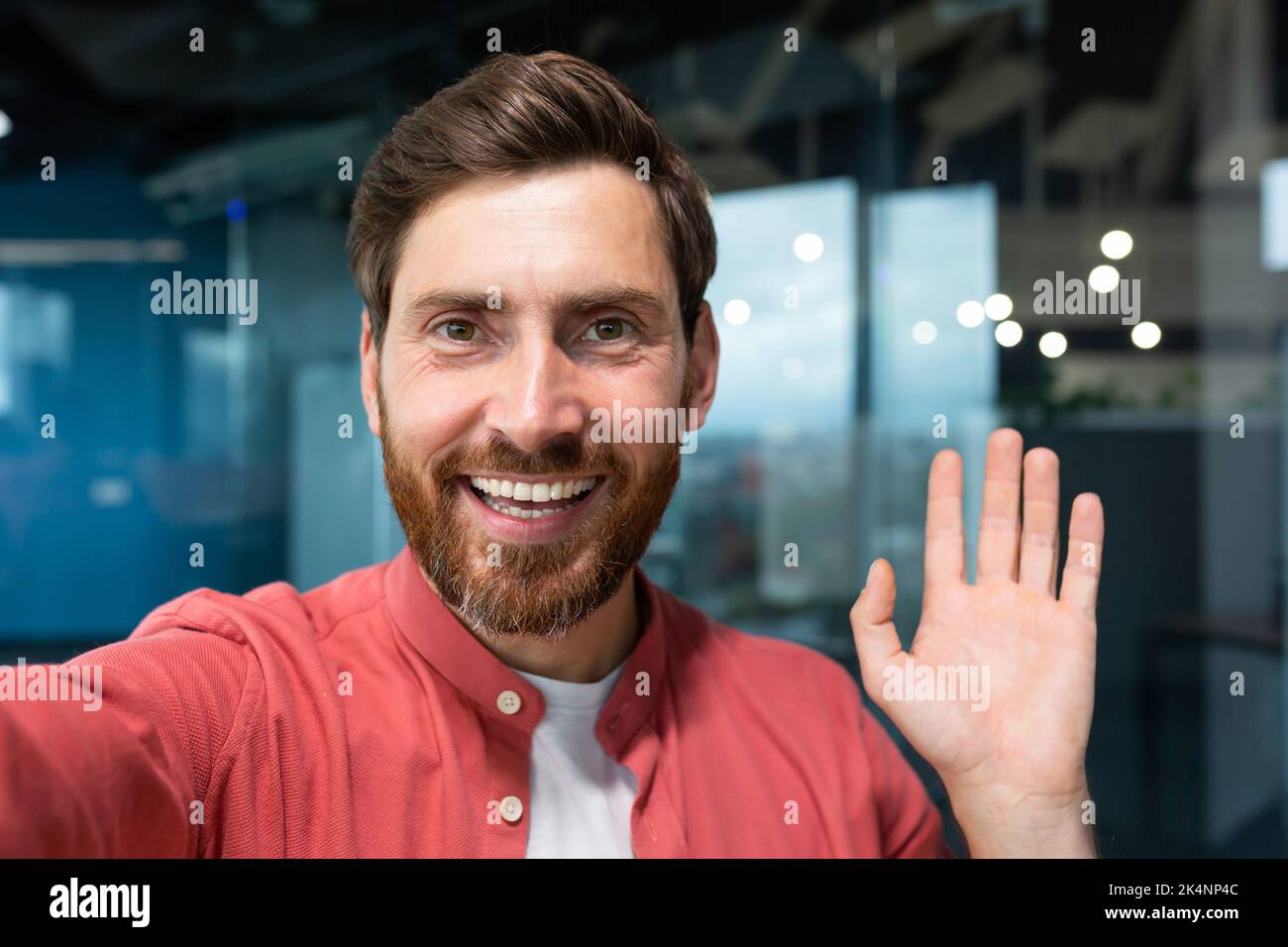 Jeune homme d'affaires heureux regardant la caméra de smartphone et parlant sur la vidéo, homme travaillant dans un immeuble de bureau moderne, souriant et parlant à distance avec des amis, à l'aide de l'application de communication. Banque D'Images