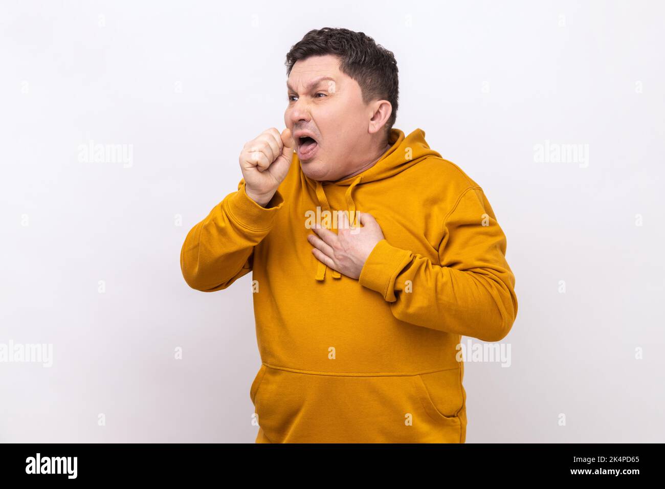 Portrait d'un homme d'âge moyen malsain toussant, attrape froid, ayant une température élevée, ayant un symptôme de grippe, portant un pull à capuche de style urbain. Studio d'intérieur isolé sur fond blanc. Banque D'Images