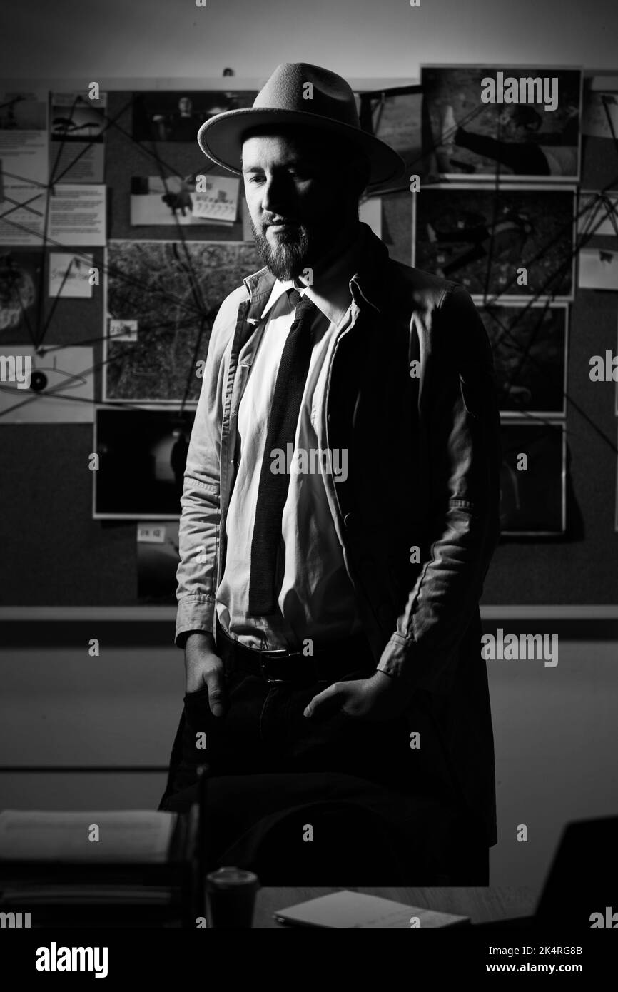 Détective privé en trench-coat et chapeau au bureau la nuit, travail de détective. Photo en noir et blanc Banque D'Images