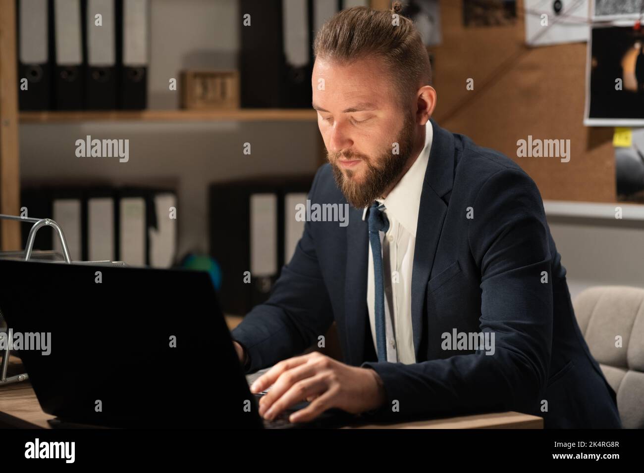 Le détective traite les preuves au bureau à l'aide d'un ordinateur qui travaille à son bureau la nuit Banque D'Images