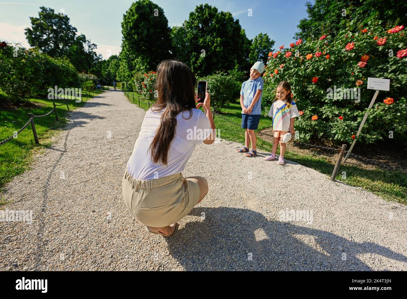 Mère prend des photos d'enfants dans le jardin sur son téléphone. Banque D'Images