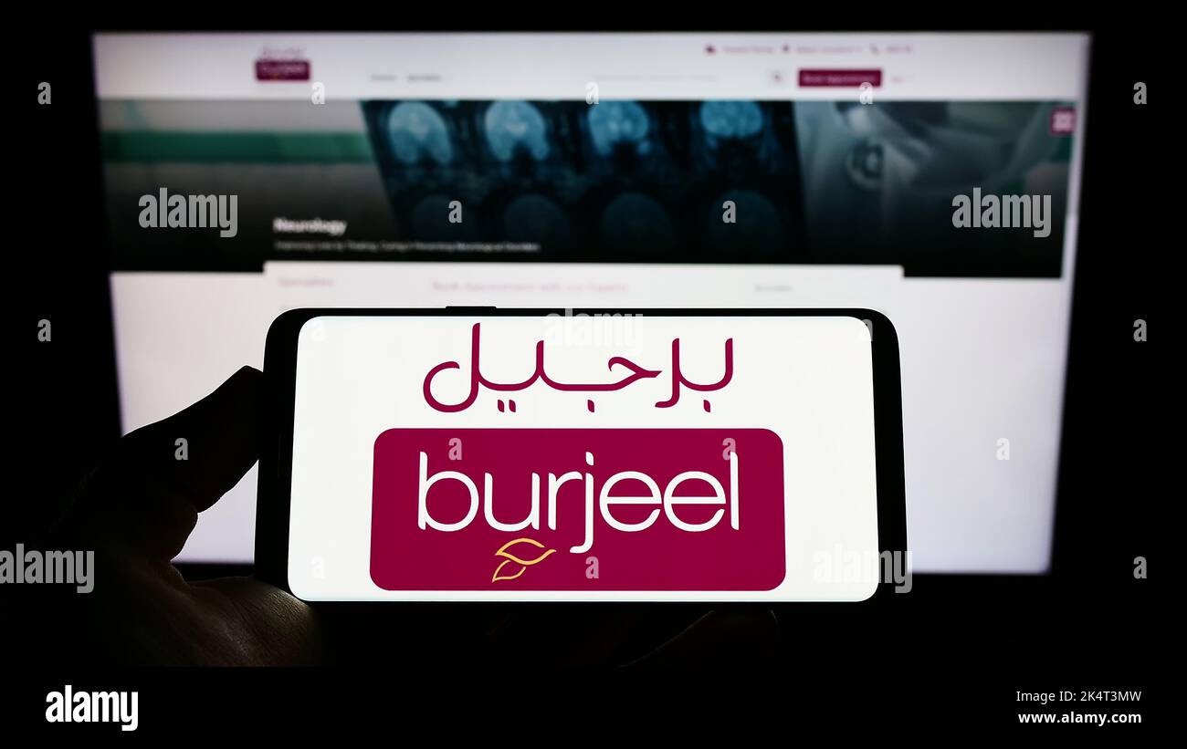 Personne tenant un téléphone portable avec le logo de l'opérateur de l'hôpital Emirati Burjeel à l'écran en face de la page Web d'affaires. Mise au point sur l'affichage du téléphone. Banque D'Images