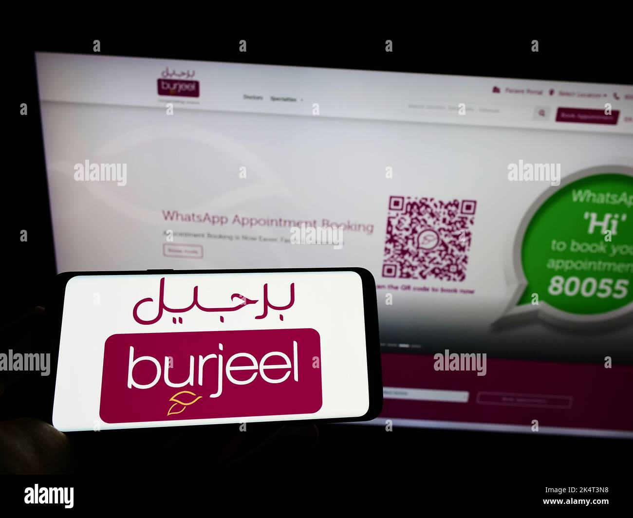 Personne tenant le téléphone portable avec le logo de l'opérateur de l'hôpital Emirati Burjeel à l'écran en face de la page web d'affaires. Mise au point sur l'affichage du téléphone. Banque D'Images