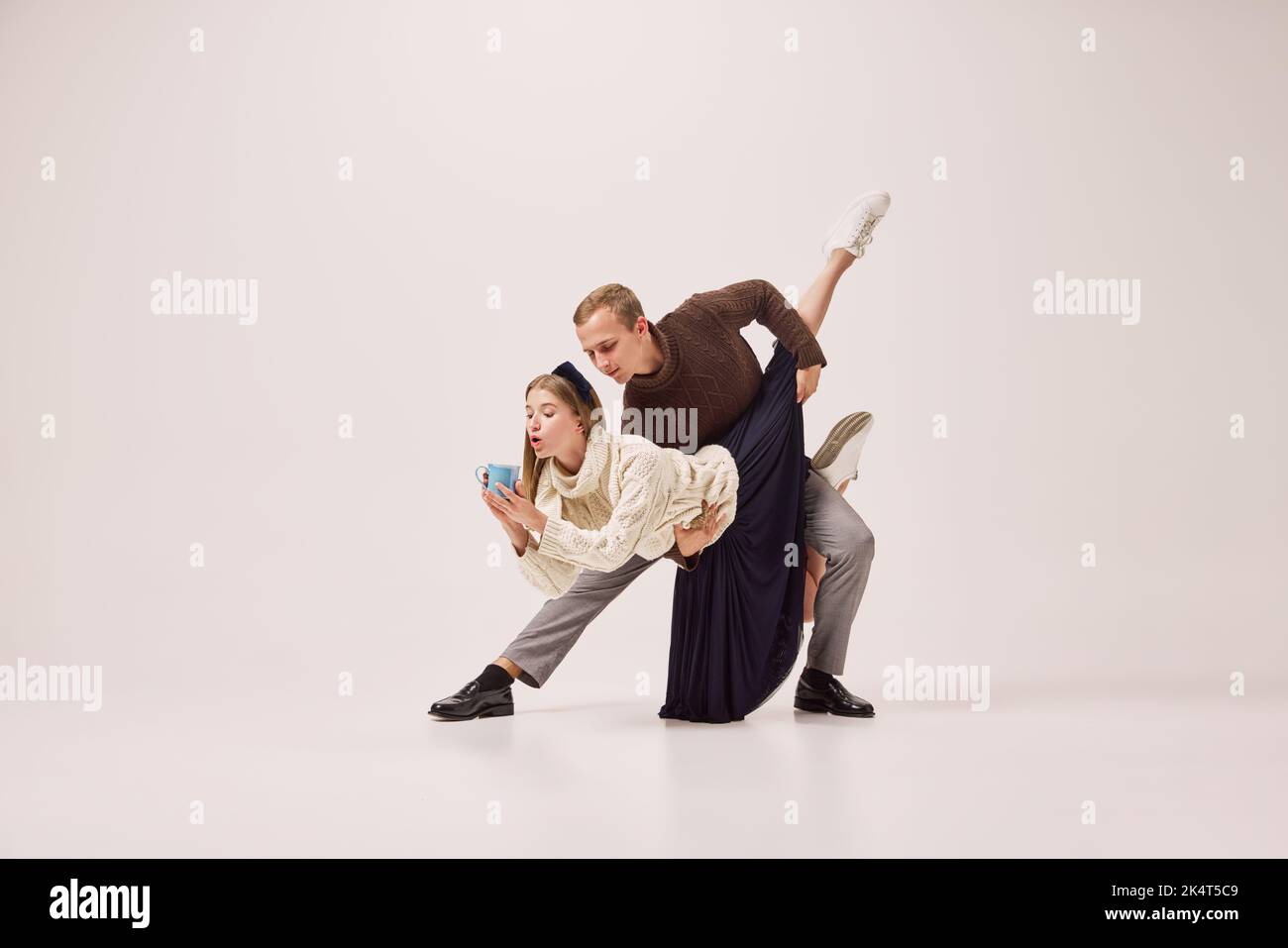 Danseurs flexibles, jeune couple heureux en vêtements d'hiver chauds dansant avec une tasse de thé chaud sur fond gris. Joyeux Noël, nouvel an, vacances Banque D'Images