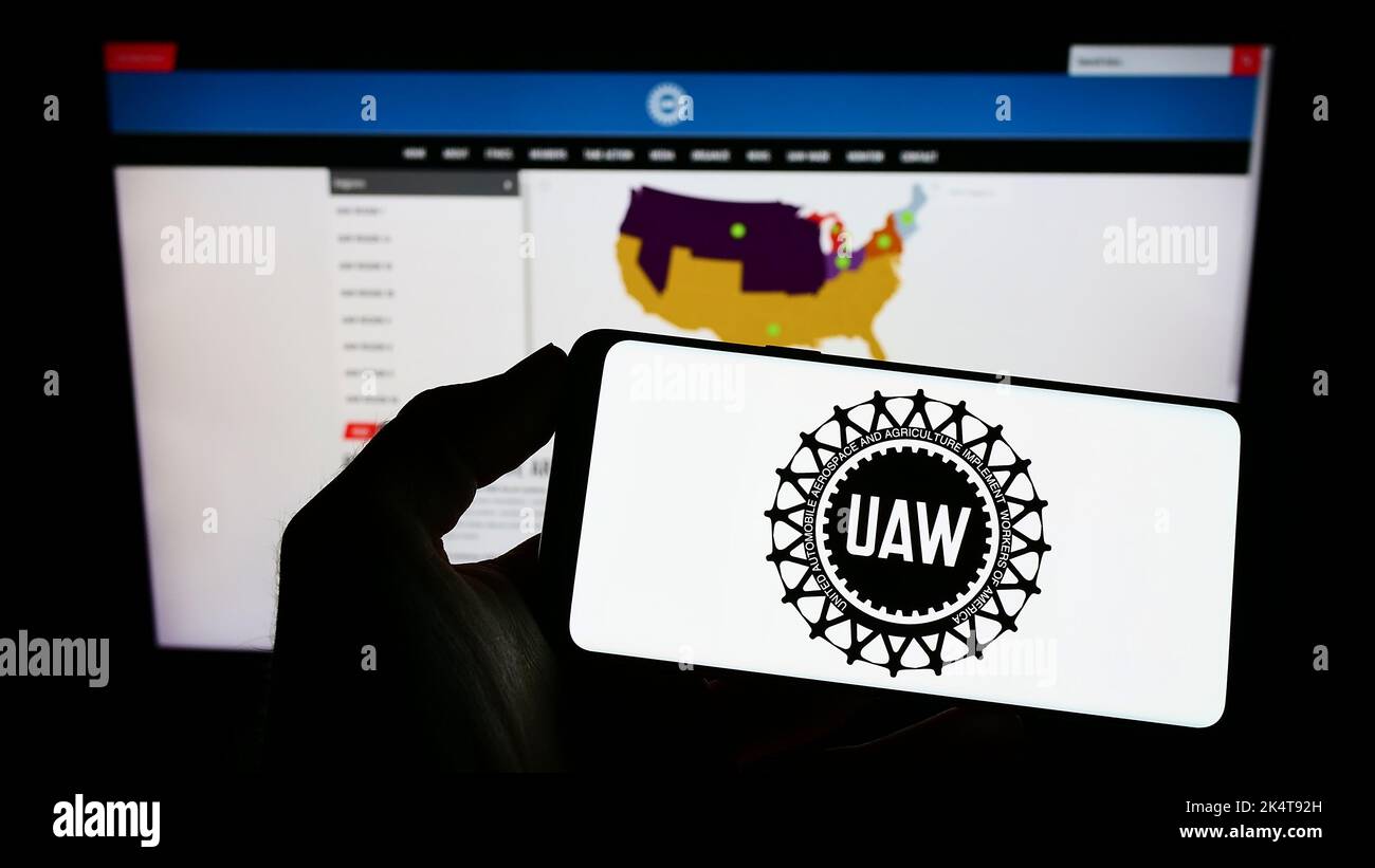 Personne tenant un téléphone portable avec le logo du syndicat américain United Auto Workers (UAW) à l'écran en face de la page Web. Mise au point sur l'affichage du téléphone. Banque D'Images