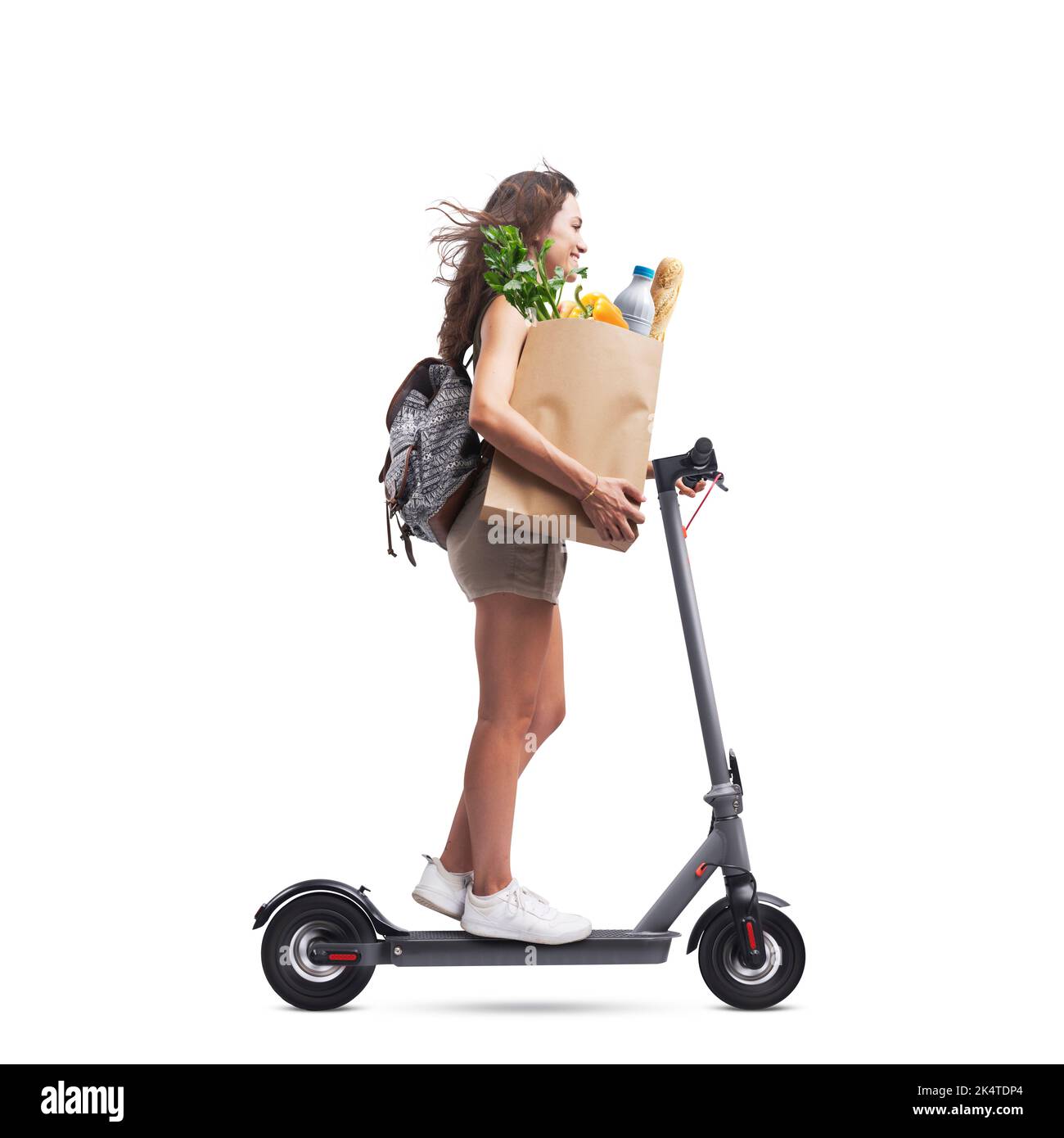 Jeune femme tenant un sac en papier avec des provisions et à cheval électrique, fond blanc Banque D'Images