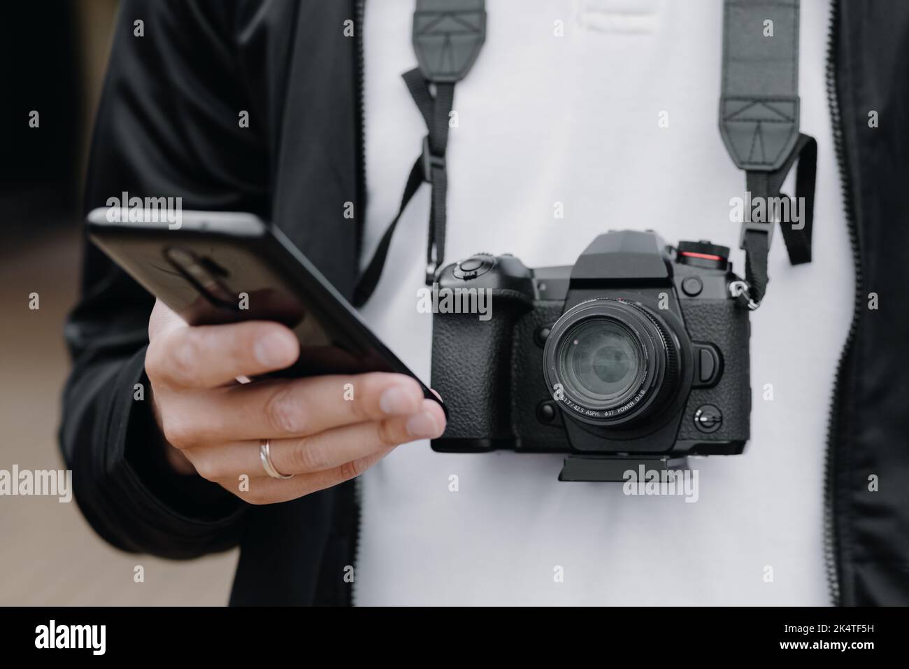 Photo d'un homme européen tenant un téléphone dans ses mains et un appareil photo autour de son cou tout en marchant à l'extérieur. Regardez le téléphone. Banque D'Images