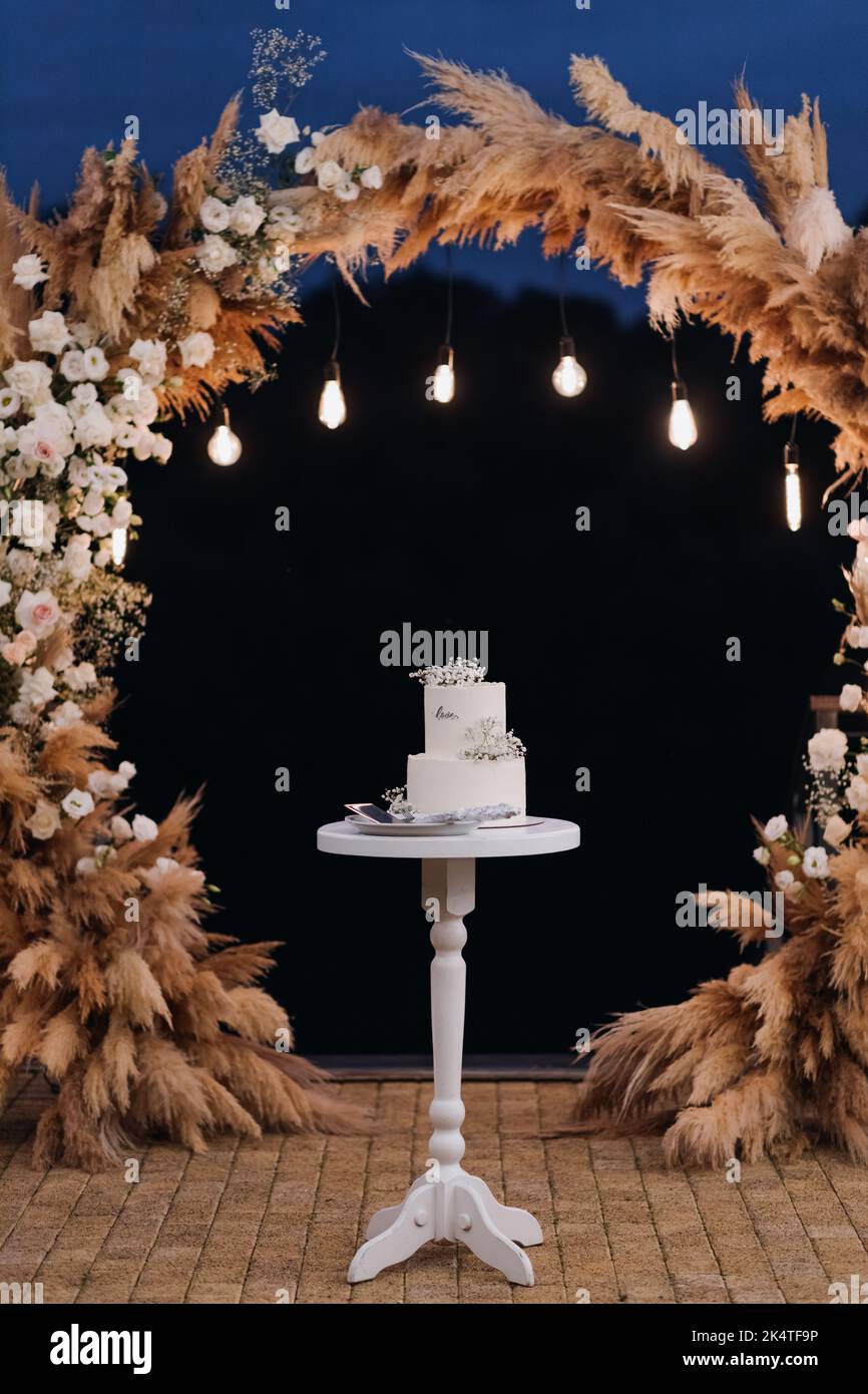 Un gâteau blanc sur un stand contre le fond d'une arche de mariage du soir Banque D'Images