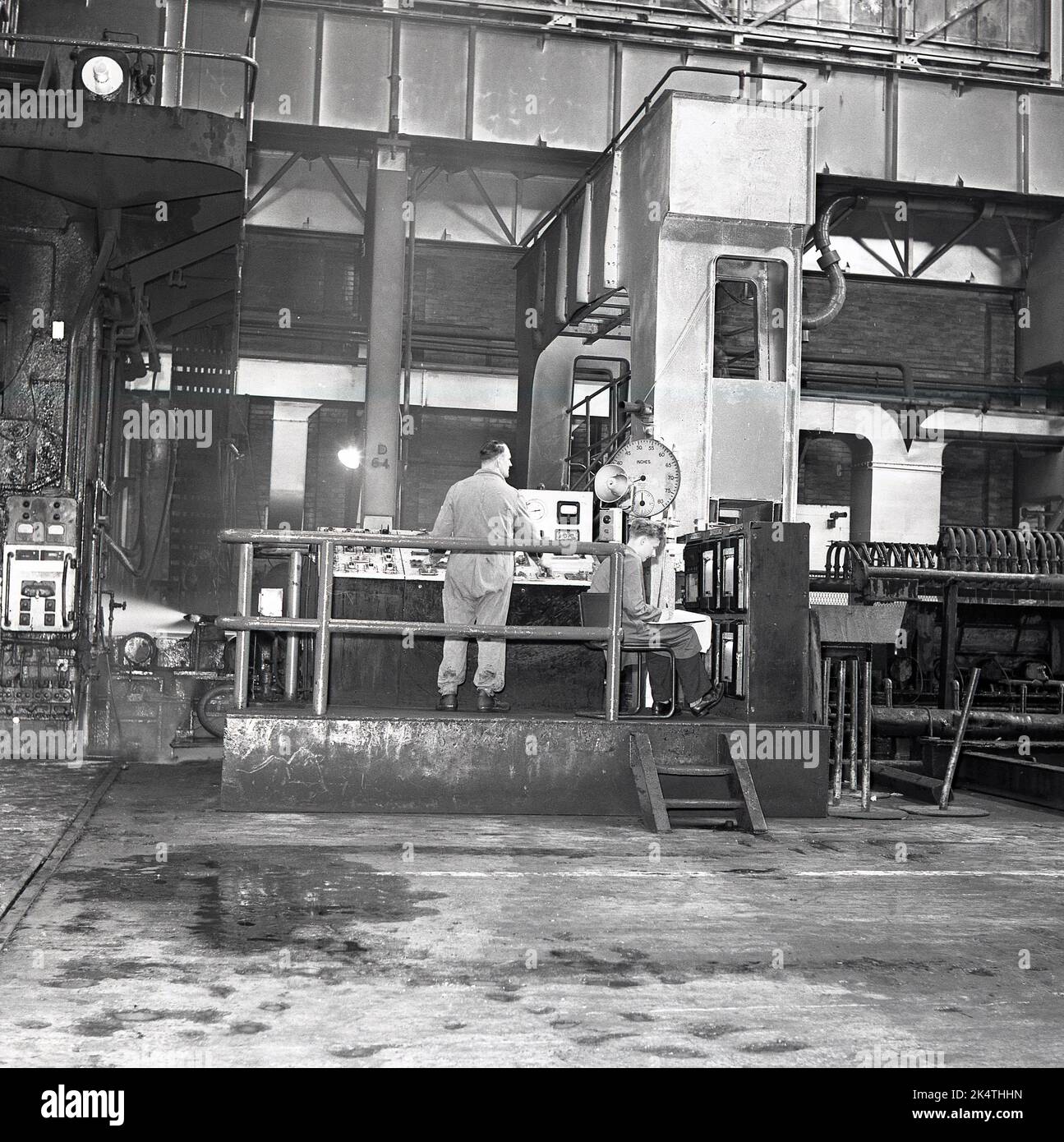 Années 1950, historique, à l'intérieur d'une aciérie, un opérateur à une unité de contrôle, et un jeune homme assis prenant des notes des lectures de données à l'Abbey Works, de la Steel Company of Wales (Scow), Port Talbot, pays de Galles, Royaume-Uni. Banque D'Images