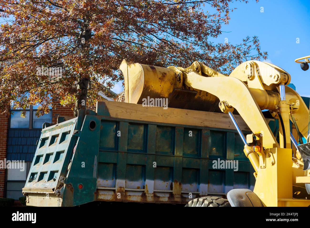 À l'approche de la saison d'automne, les employés municipaux retirent les feuilles mortes du sol près des maisons à l'aide d'un bulldozer et d'un camion Banque D'Images