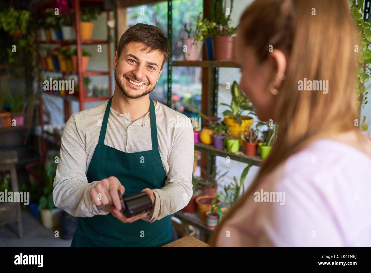 Fleuriste souriant avec lecteur NFC et client à la caisse payant dans la boutique de fleurs Banque D'Images