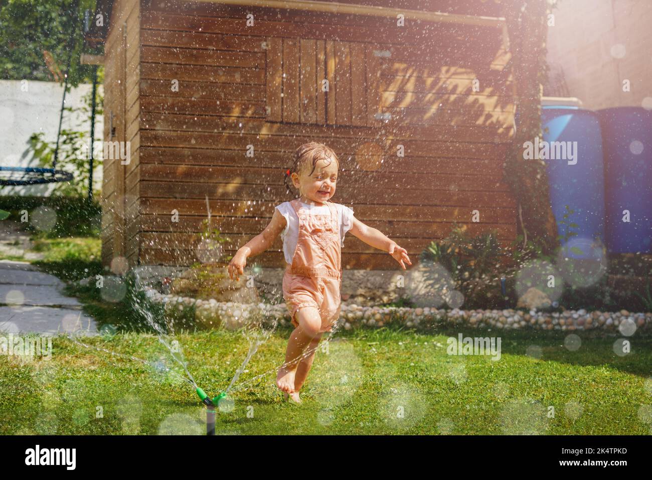 Une fille en vêtements mouillés coule autour d'un arroseur d'eau dans le jardin Banque D'Images