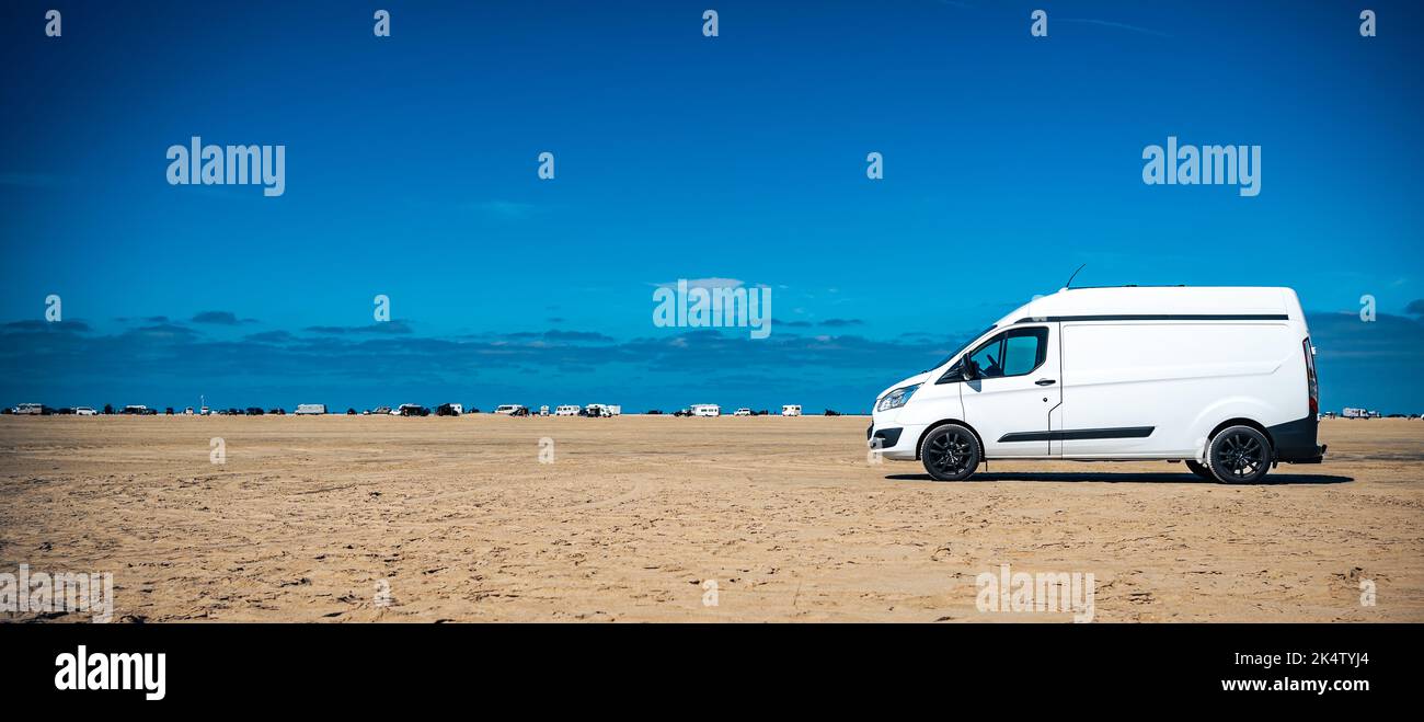 Campeur blanc à la plage lors d'une journée ensoleillée d'été avec ciel bleu et autres voitures vanlife en arrière-plan Banque D'Images