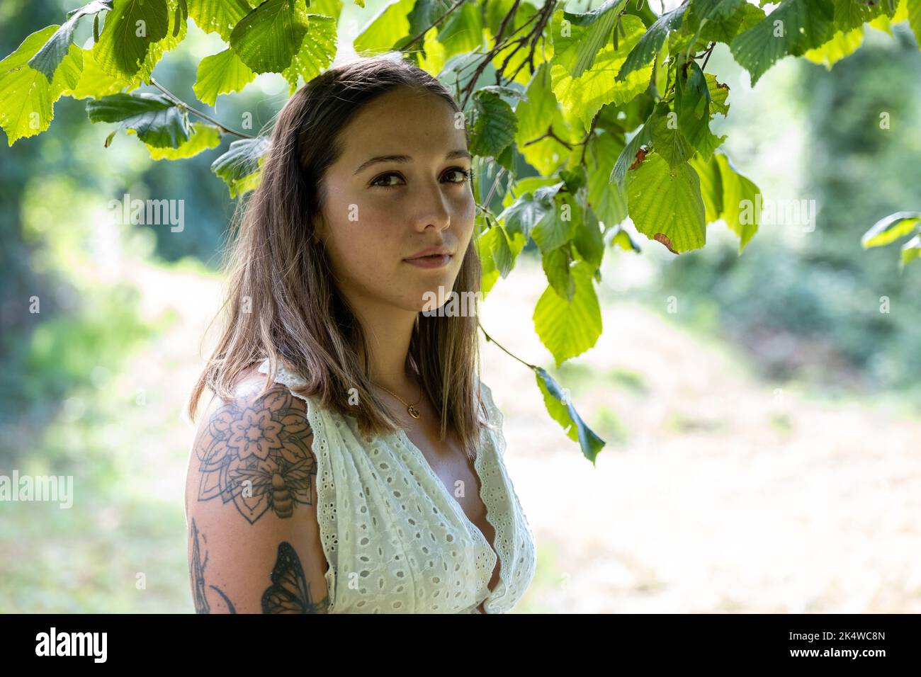 Portrait d'une jeune femme avec des tatouages debout sous un arbre en été, France Banque D'Images