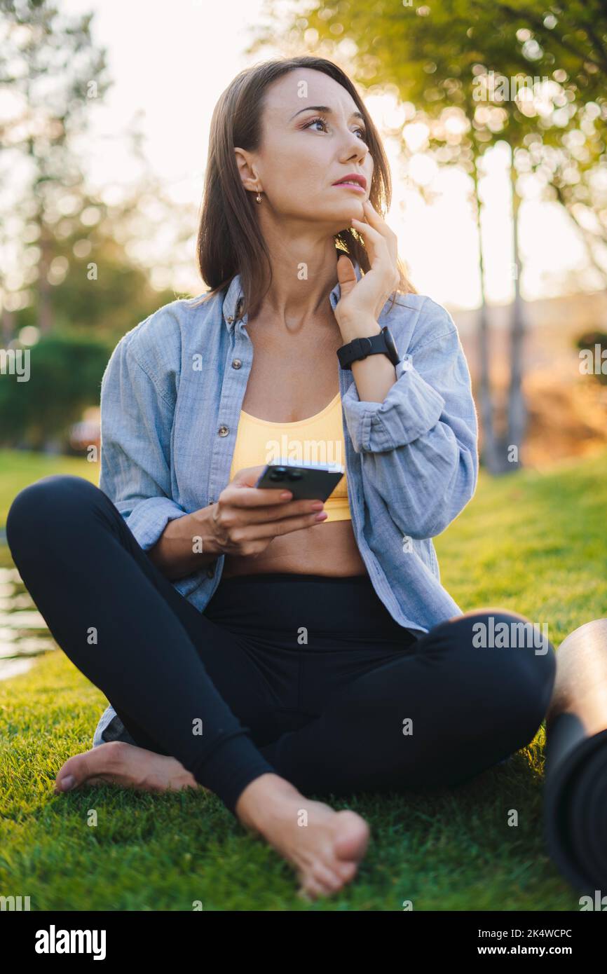Femme sportive dans les vêtements de sport regardant le tutoriel en ligne sur smartphone, pendant l'entraînement matinal dans le parc. Femme sportive et active de race blanche. En bonne santé Banque D'Images