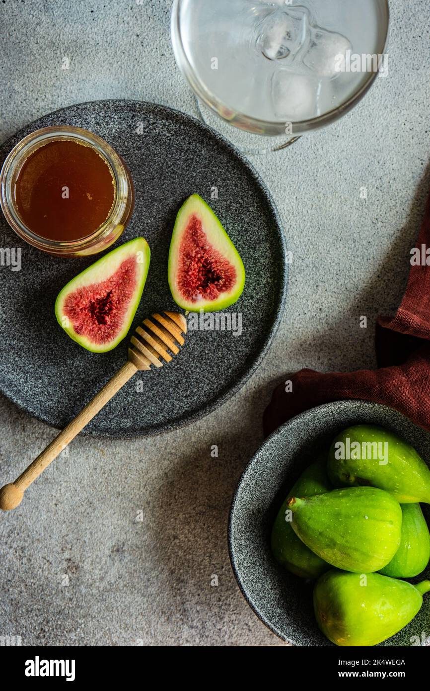 Vue aérienne d'une assiette de figues vertes mûres sur une assiette avec miel et un verre d'eau glacée Banque D'Images