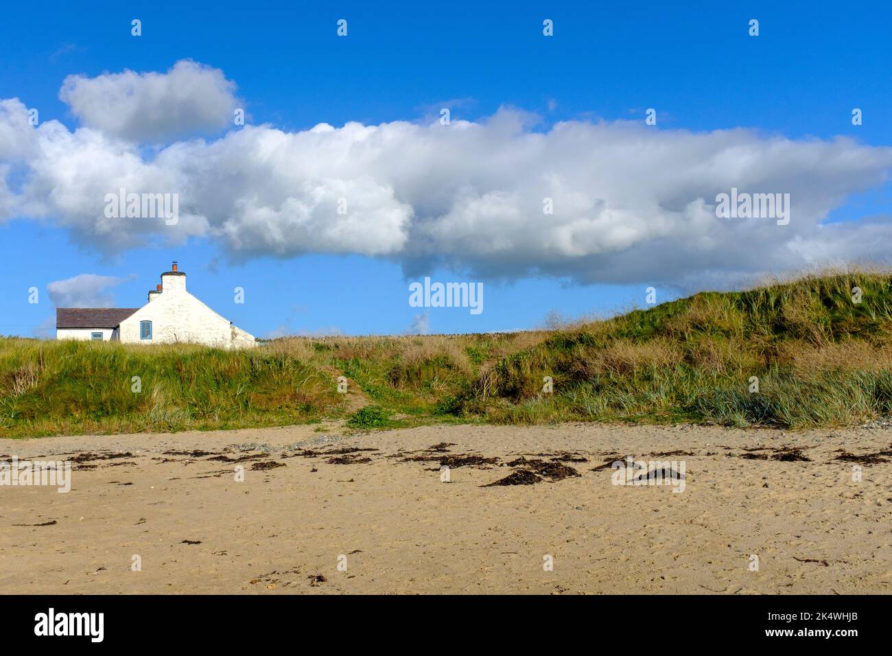 Nuages blancs dans un ciel bleu clair au-dessus d'un simple cottage au-dessus des dunes de sable à Rhosneigr, au nord du pays de Galles, au Royaume-Uni Banque D'Images