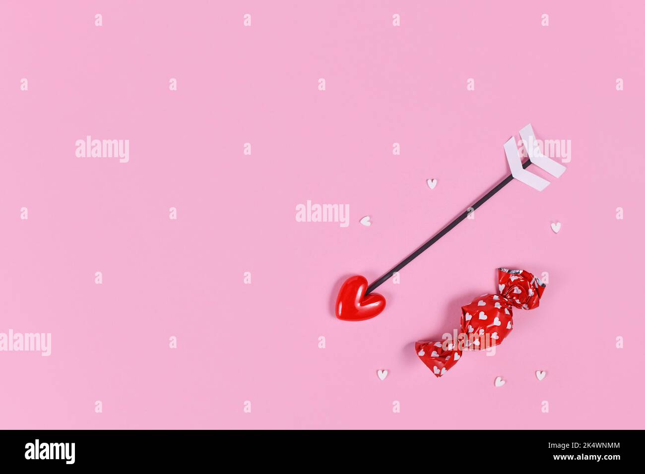Candy rouge avec petits coeurs et flèche d'amour sur fond rose avec espace de copie Banque D'Images