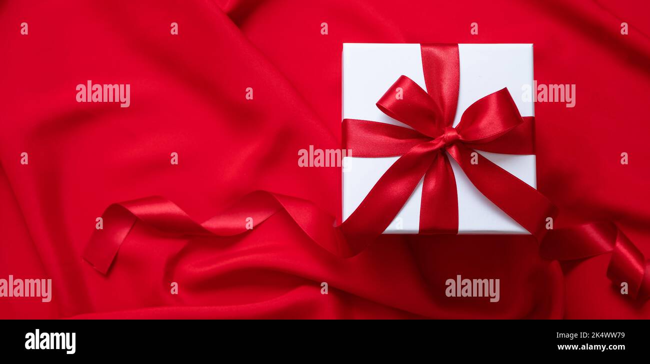 Gift Saint-Valentin, cadeau de Noël. Dessus de boîte blanche avec ruban rouge et boucle sur fond satiné, décoration en boucle Banque D'Images