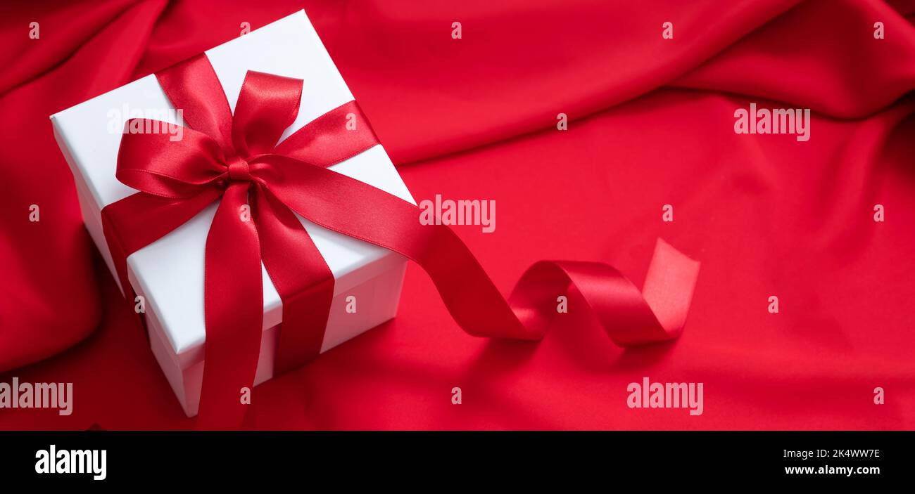 Boîte cadeau blanche avec ruban rouge et noeud sur fond satiné.Noël Saint-Valentin présent, décoration curly Banque D'Images