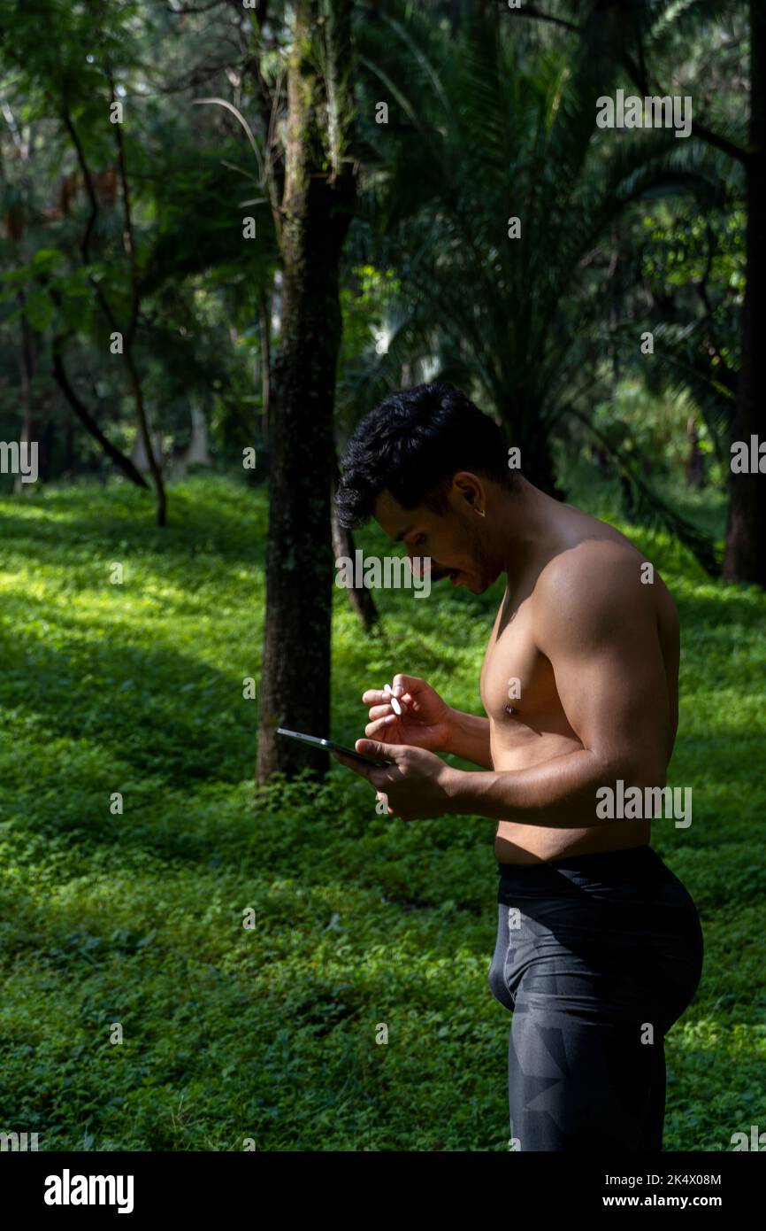 Des yogi masculins actifs et beaux se promène dans un parc en forêt avant ou après un entraînement. Jeune homme sportif hispanique, cours de yoga avec tapis de fitness Banque D'Images