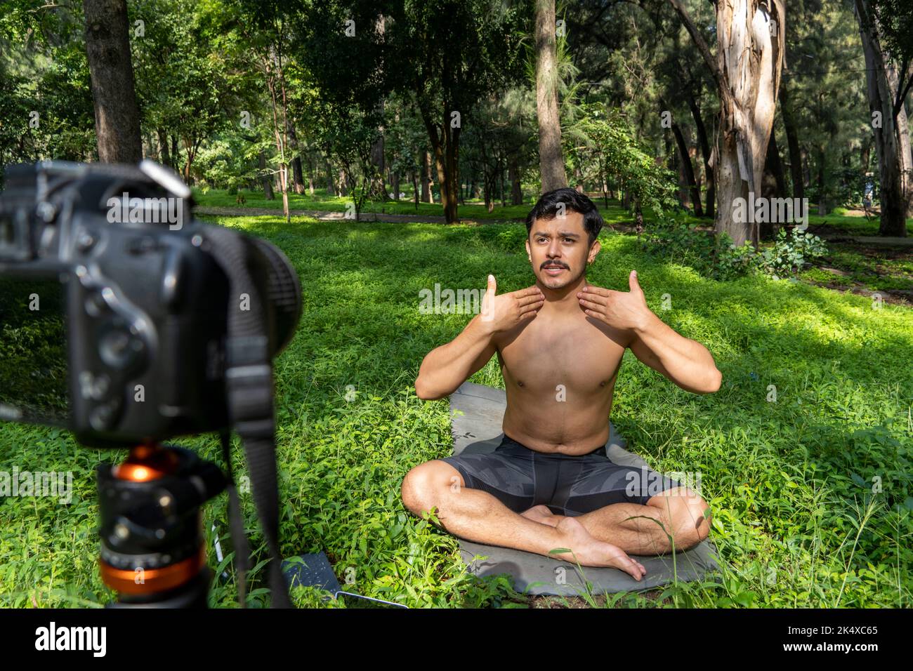 Jeune homme pratiquant le yoga asana, équilibre, méditant en se tenant sur une jambe sur tapis de sport sur l'herbe verte dans le parc. Utilisation de la tablette pour les cours en ligne. Banque D'Images
