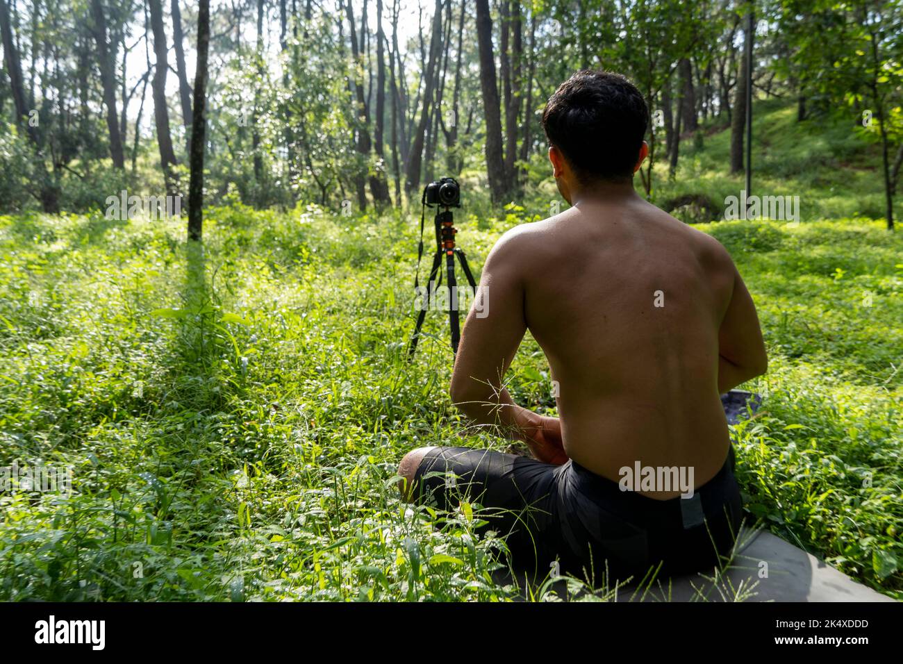 Jeune homme pratiquant le yoga asana, équilibre, méditant en se tenant sur une jambe sur tapis de sport sur l'herbe verte dans le parc. Utilisation de la tablette pour les cours en ligne. Banque D'Images