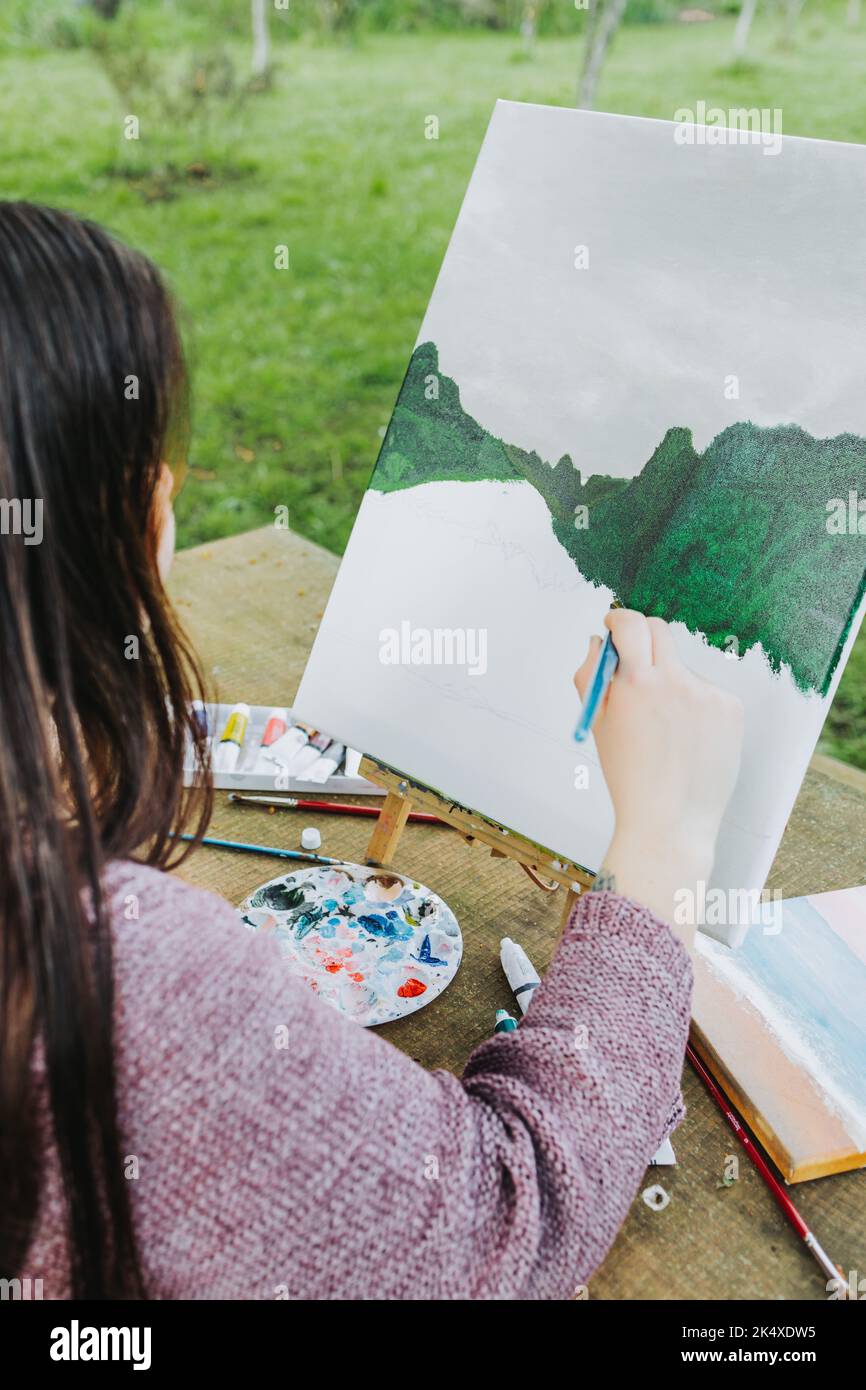 Jeune artiste méconnaissable peignant son propre paysage de montagne avec de l'huile sur une toile. Peintre amateur. Banque D'Images