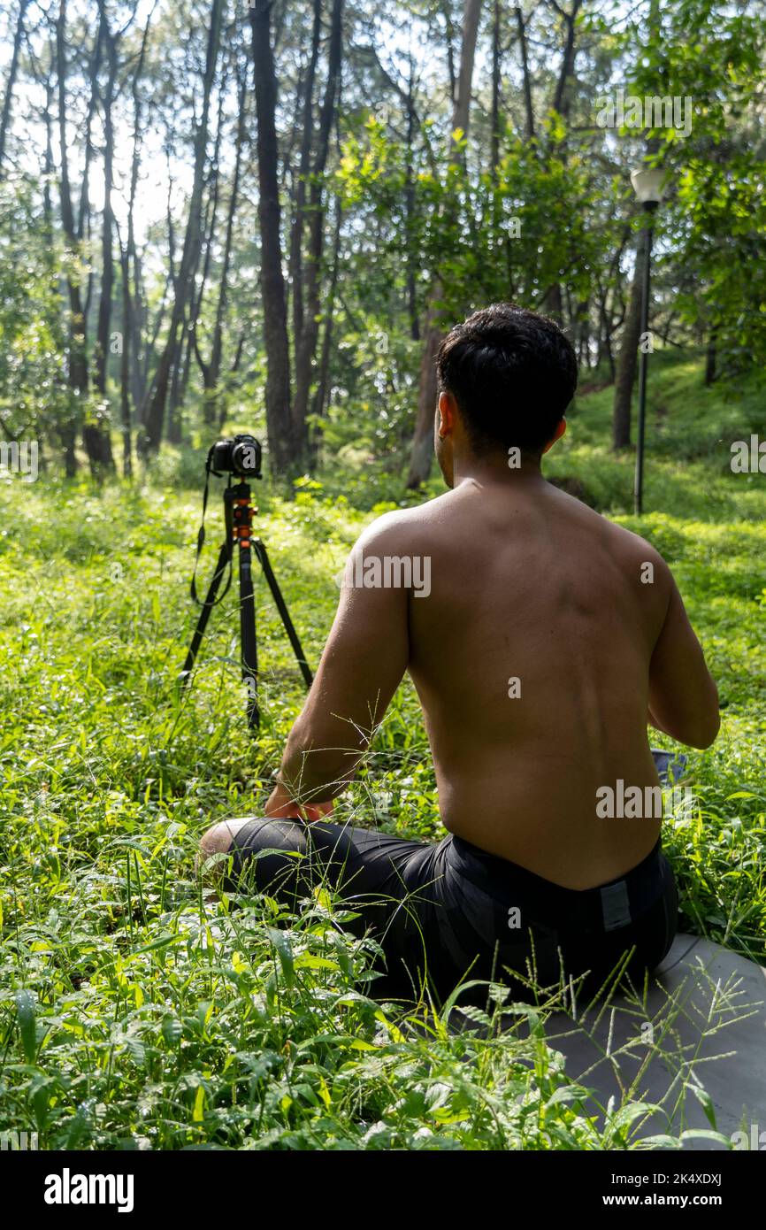 Jeune homme pratiquant le yoga asana, équilibre, méditant en se tenant sur une jambe sur tapis de sport sur l'herbe verte dans le parc. Utilisation de la tablette pour les cours en ligne. Banque D'Images