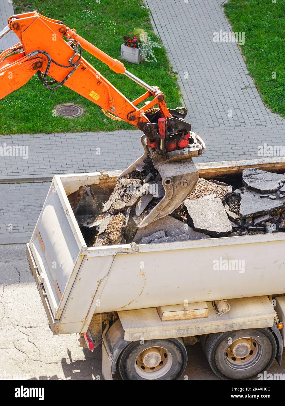 Une pelle hydraulique orange équipée d'un godet charge les anciens morceaux d'asphalte dans un camion à benne blanche Banque D'Images