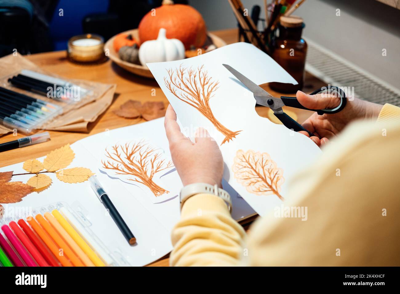 Artisanat d'automne pour adultes. Portrait sans visage d'une femme dessinant des arbres d'automne avec des marqueurs et coupant le collage du papier. Banque D'Images