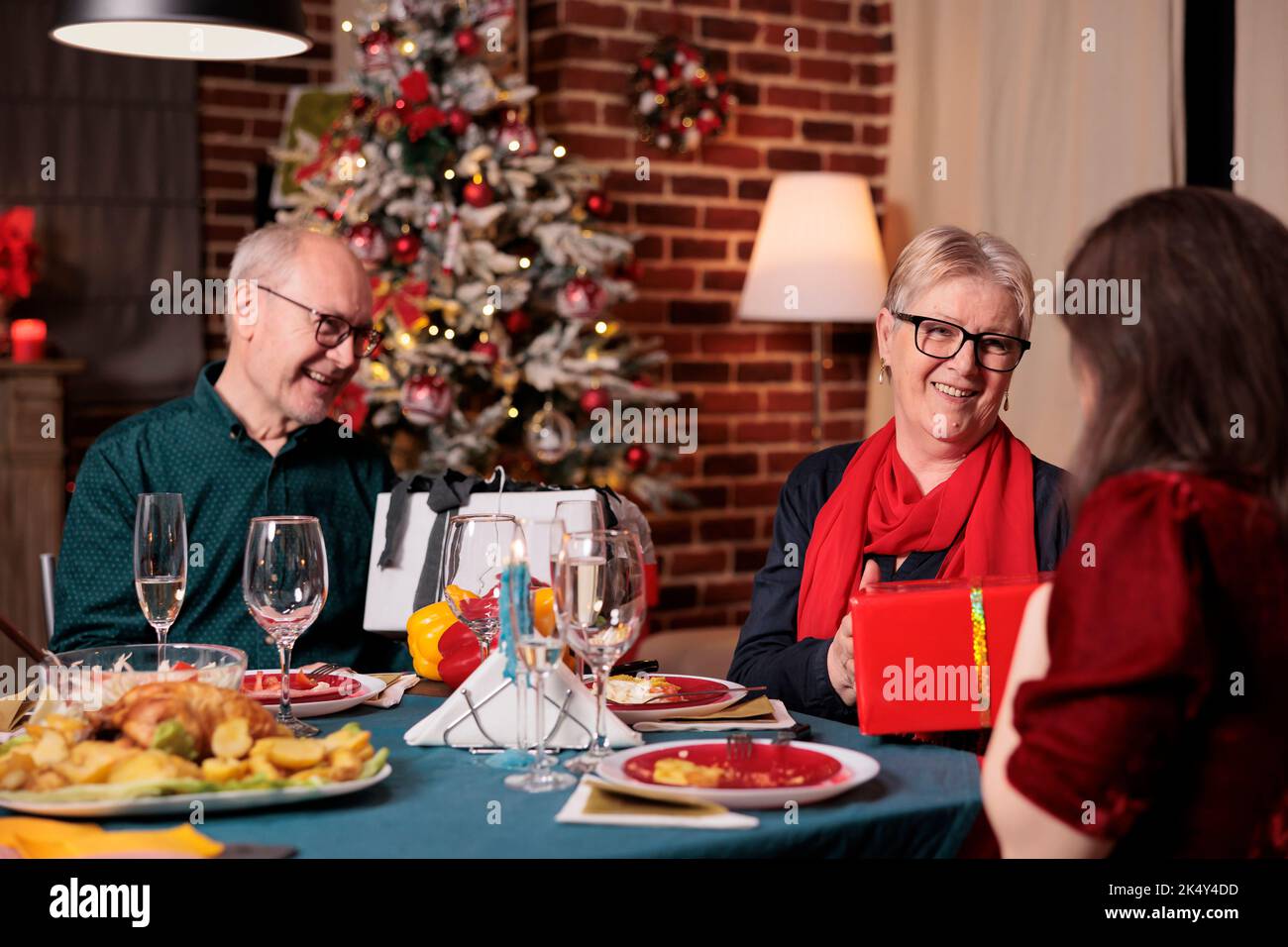 Famille échangeant des cadeaux de noël à la table de fête, célébrant Noël ensemble, dîner. Fête des vacances d'hiver avec les parents, la fille donnant des cadeaux à maman et papa Banque D'Images