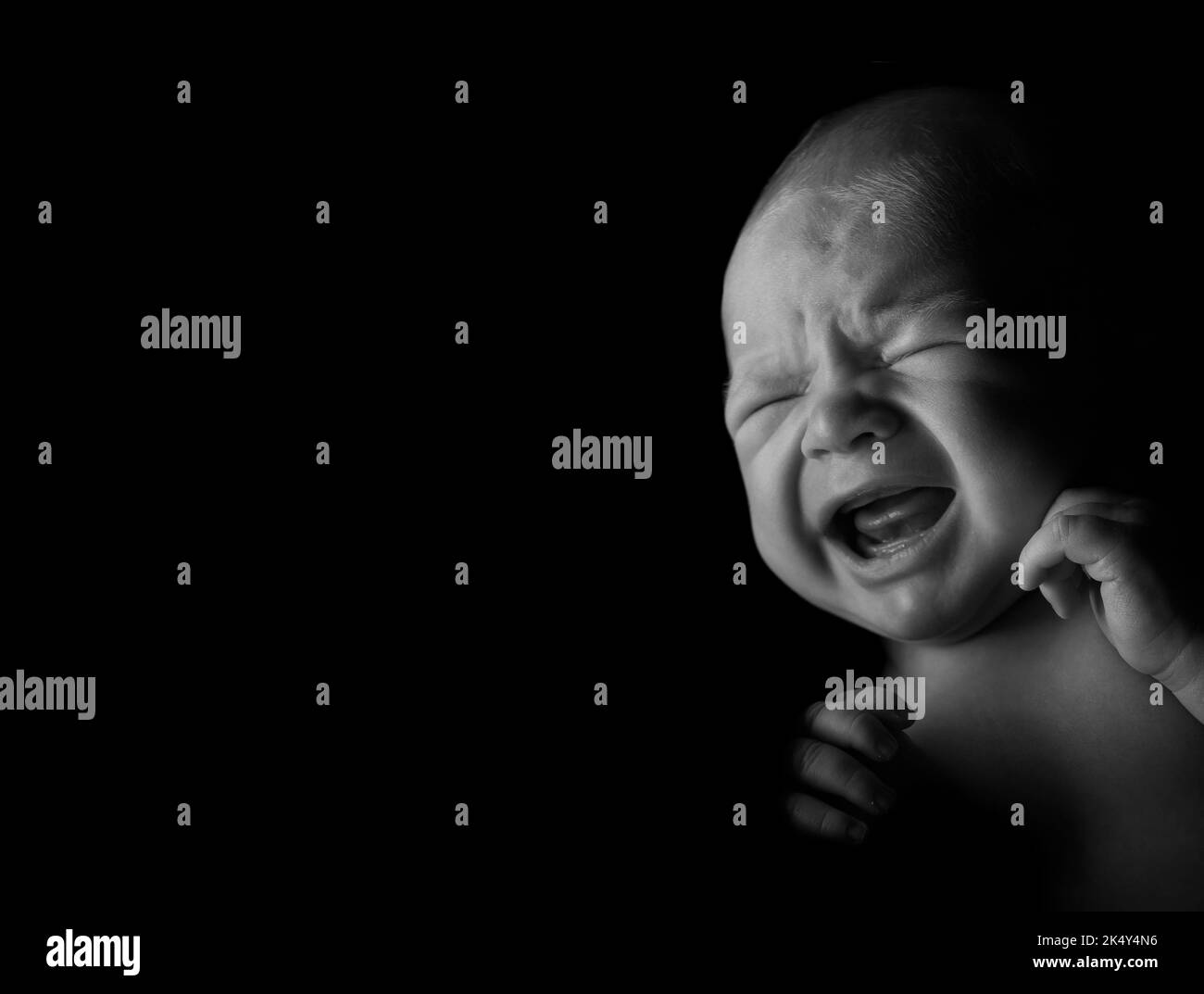 Bébé garçon pleure, lumière studio utilisée sur fond noir. Banque D'Images