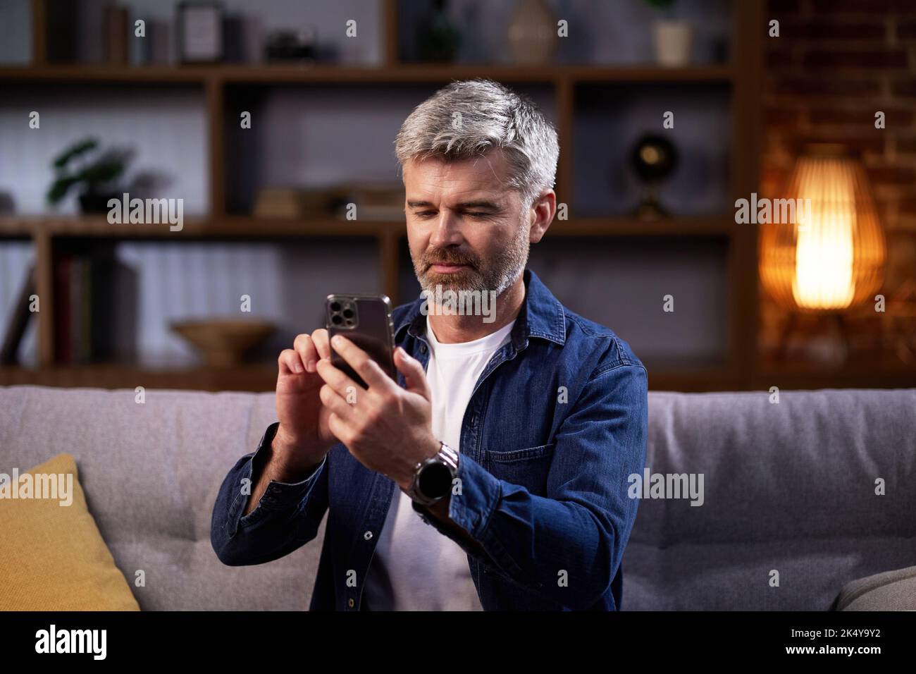 Homme souriant communique en ligne sur les réseaux sociaux et utilise un smartphone. Un homme en vêtements décontractés regarde à travers un téléphone mobile, communique dans un Banque D'Images