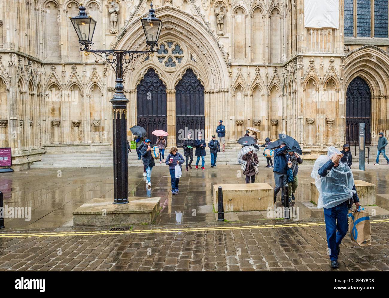 Les touristes et les visiteurs se protègent de la pluie en utilisant des parasols et des manteaux de pluie sur les rues humides près de la cathédrale de York. Banque D'Images