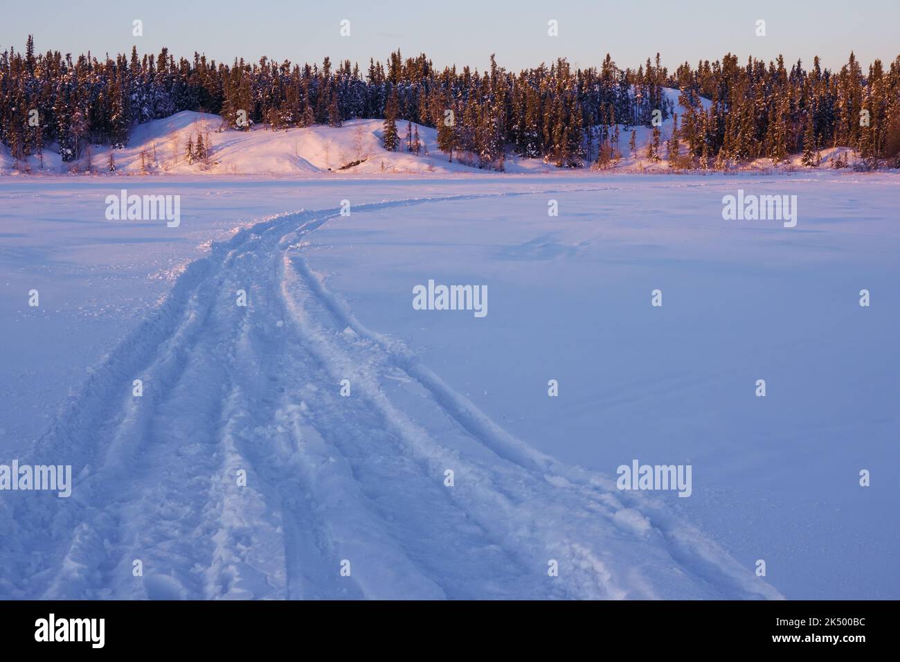 Lever du soleil à Frame Lake, à Yellowknife, Canada, marqué par les pistes de personnes qui pratiquent des sports d'hiver dans l'environnement gelé. Banque D'Images