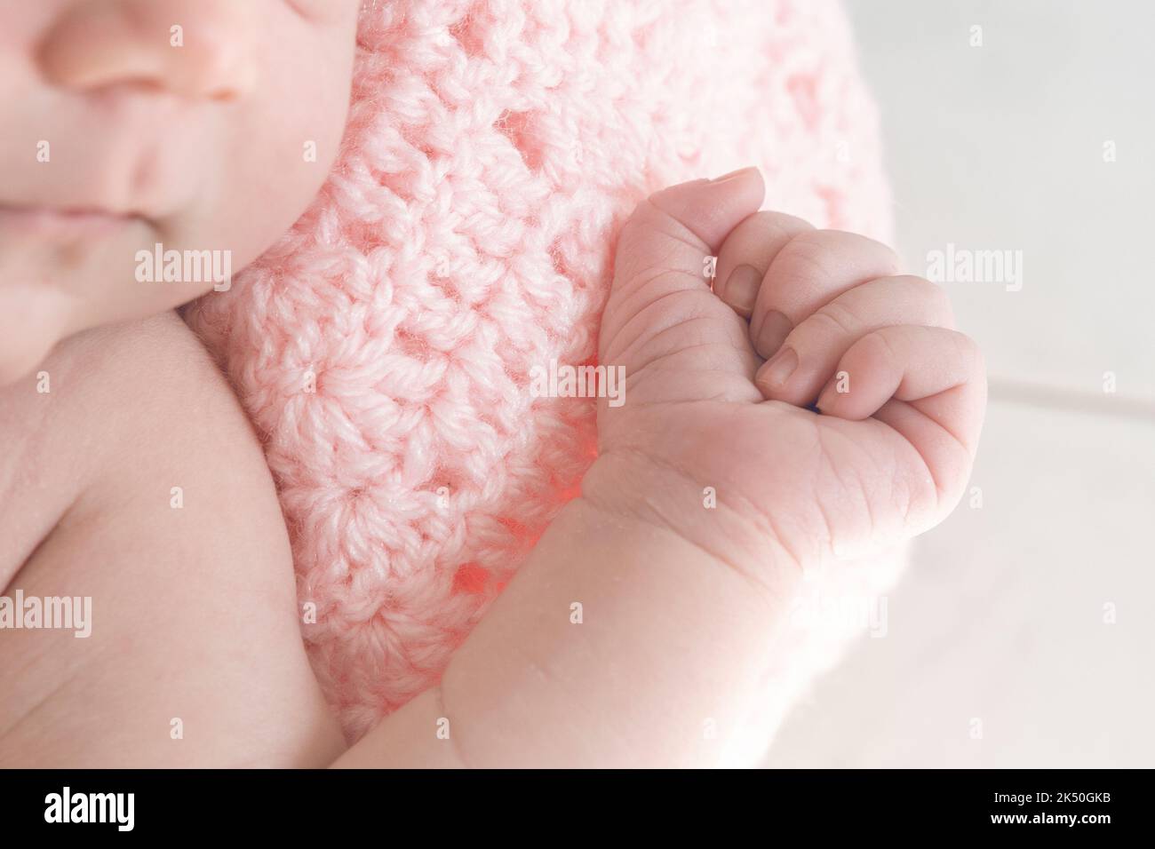 Détail de la main d'une petite fille enveloppée dans une couverture en laine rose Banque D'Images