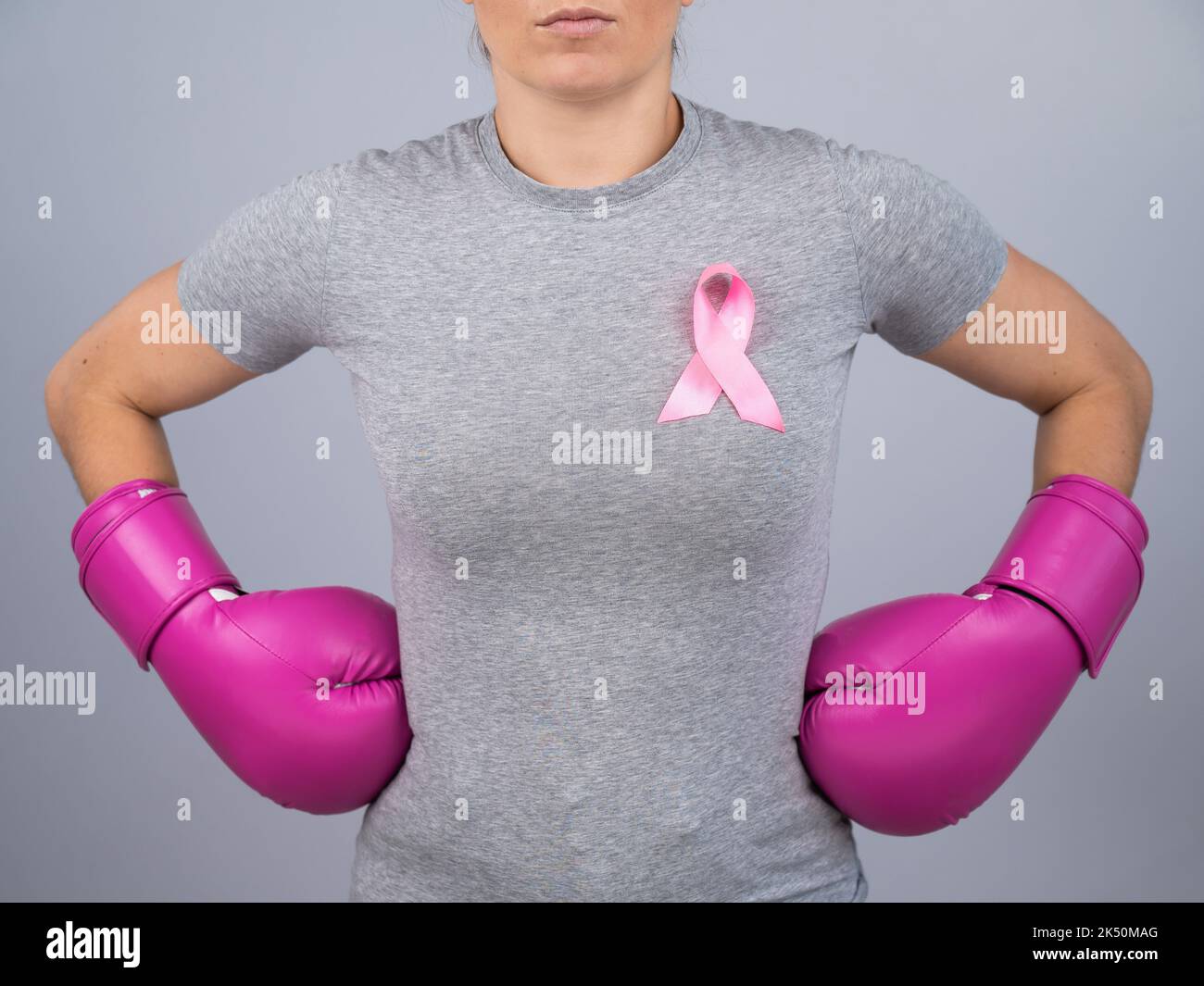 Une femme sans visage en gants de boxe rose avec un ruban rose tient ses mains au niveau des hanches. Lutte contre le cancer du sein. Banque D'Images Une femme sans visage en gants de boxe rose avec un ruban rose tient ses mains au niveau des hanches. Lutte contre le cancer du sein. Banque D'Images