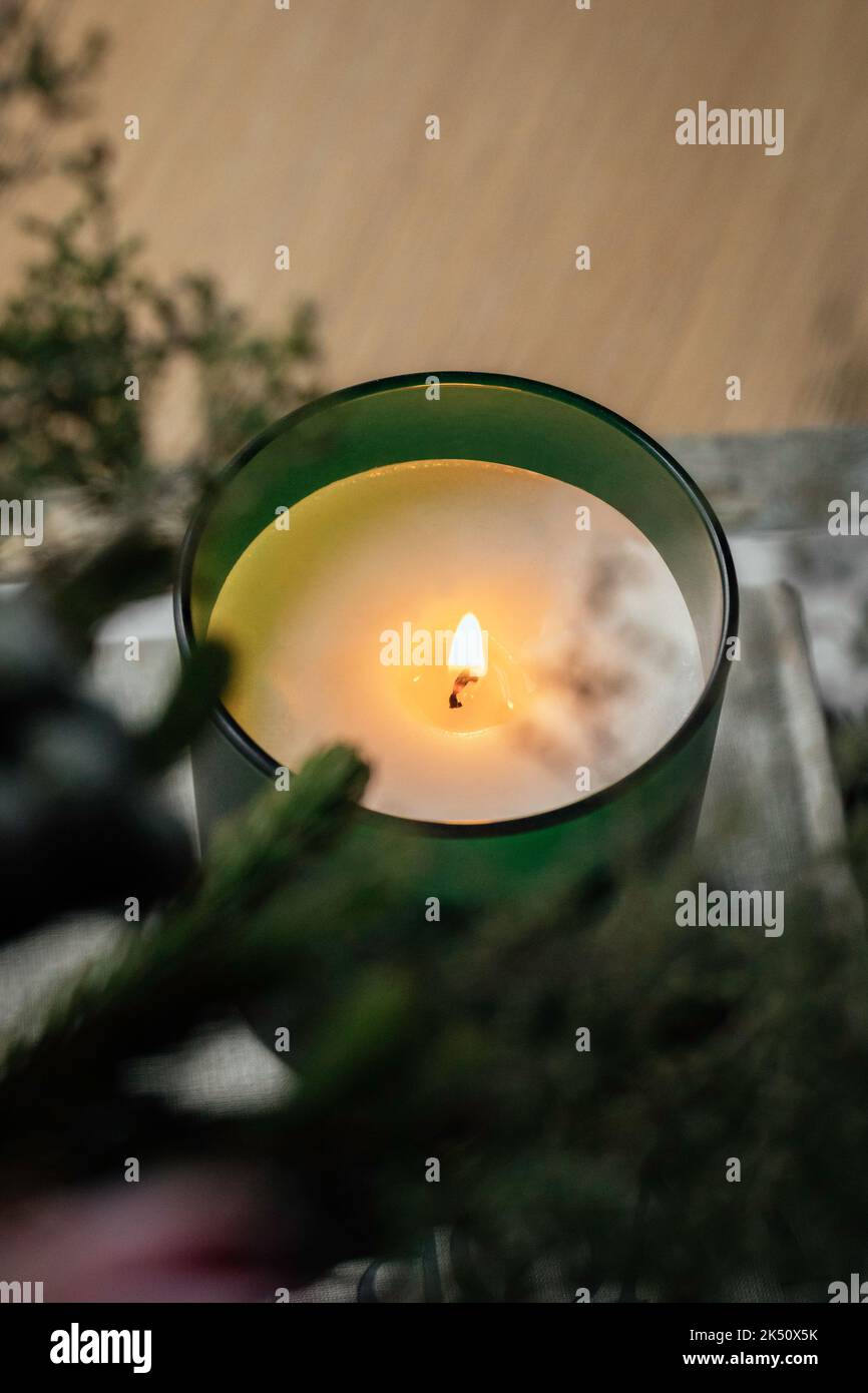 Bougie de soja dans un pot en verre vert assis sur une pile de livres dans la chambre parmi les fleurs automnales Banque D'Images