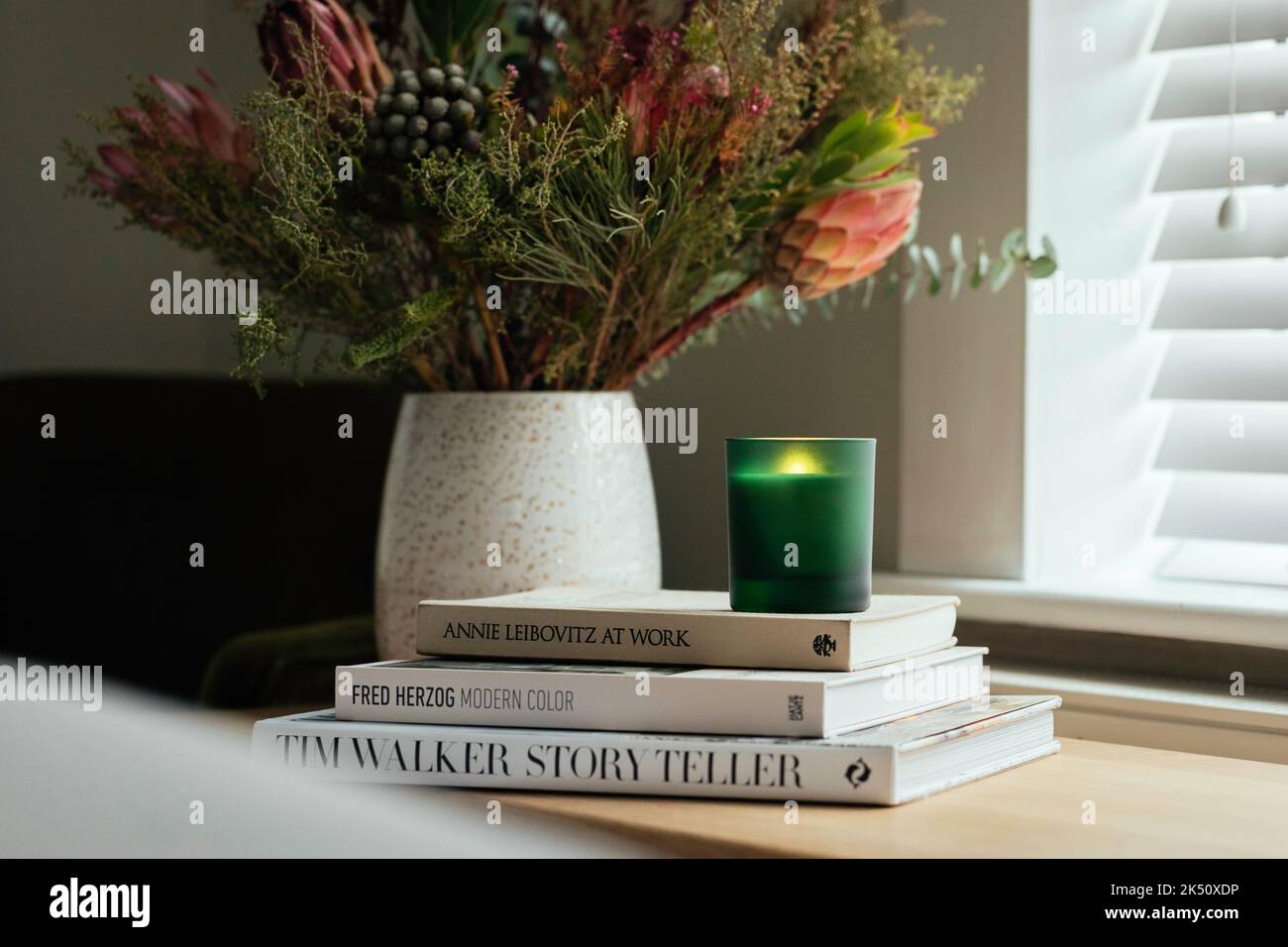 Bougie de soja dans un pot en verre vert assis sur une pile de livres dans la chambre parmi les fleurs automnales Banque D'Images