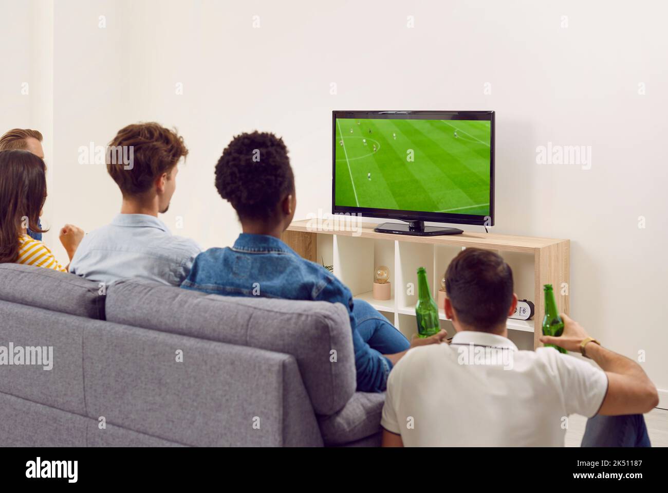 Groupe d'amis divers assis sur un canapé, regardant le football à la télévision et buvant de la bière Banque D'Images