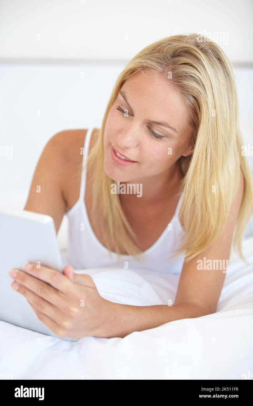 Vérifier son courrier avant de travailler. Une belle jeune femme blonde travaillant sur son pavé numérique tout en étant couché dans le lit. Banque D'Images