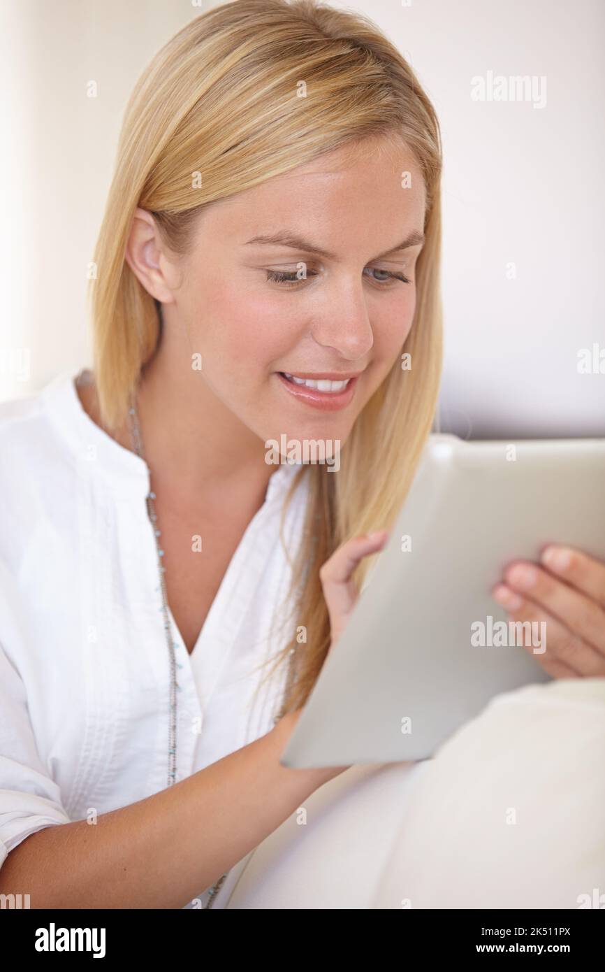 Lire son livre préféré en ligne. Une belle jeune femme blonde travaillant sur son pavé numérique. Banque D'Images