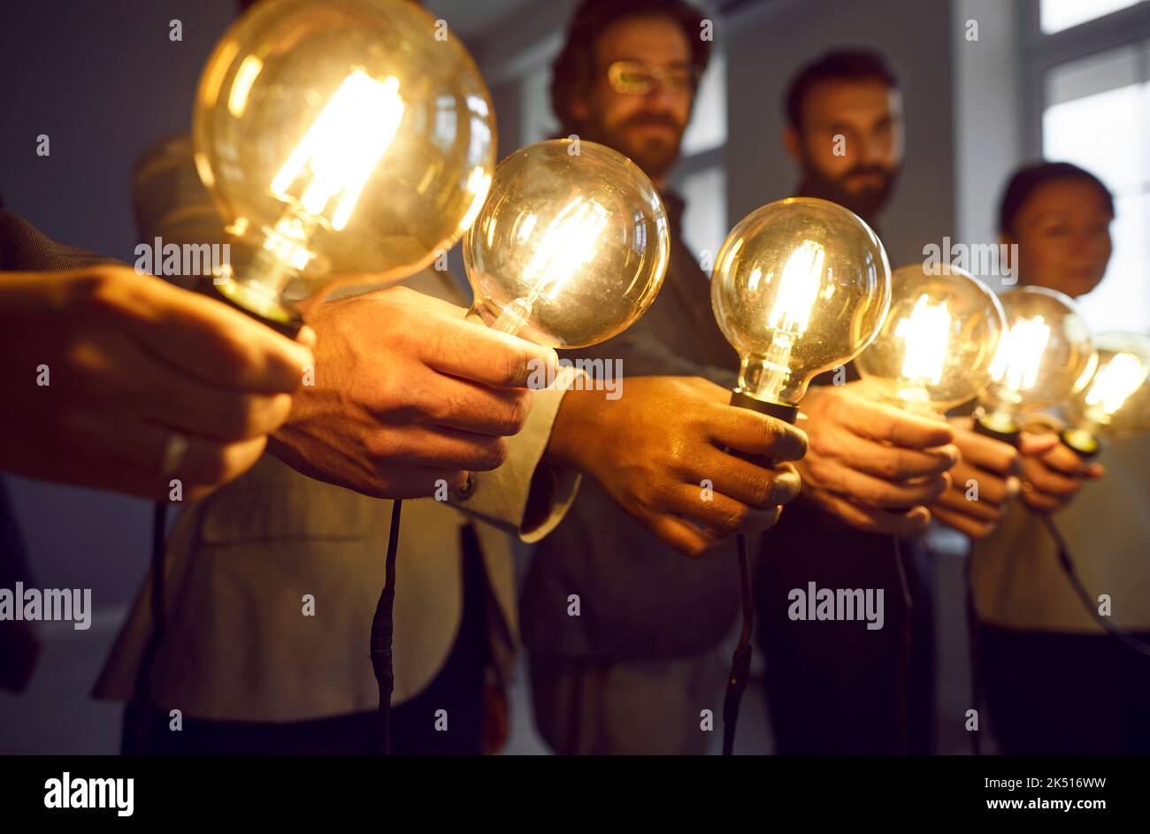 Des ampoules lumineuses aux mains de l'équipe d'affaires créative au bureau comme symboles de leurs idées. Banque D'Images