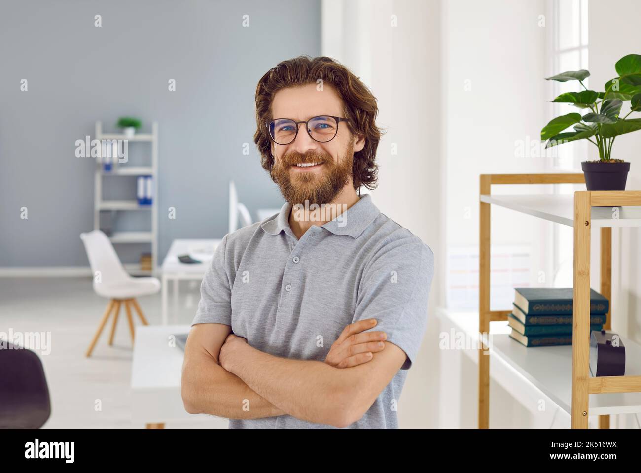Homme caucasien confiant avec une barbe souriante regardant la caméra posant avec des bras croisés dans le bureau Banque D'Images
