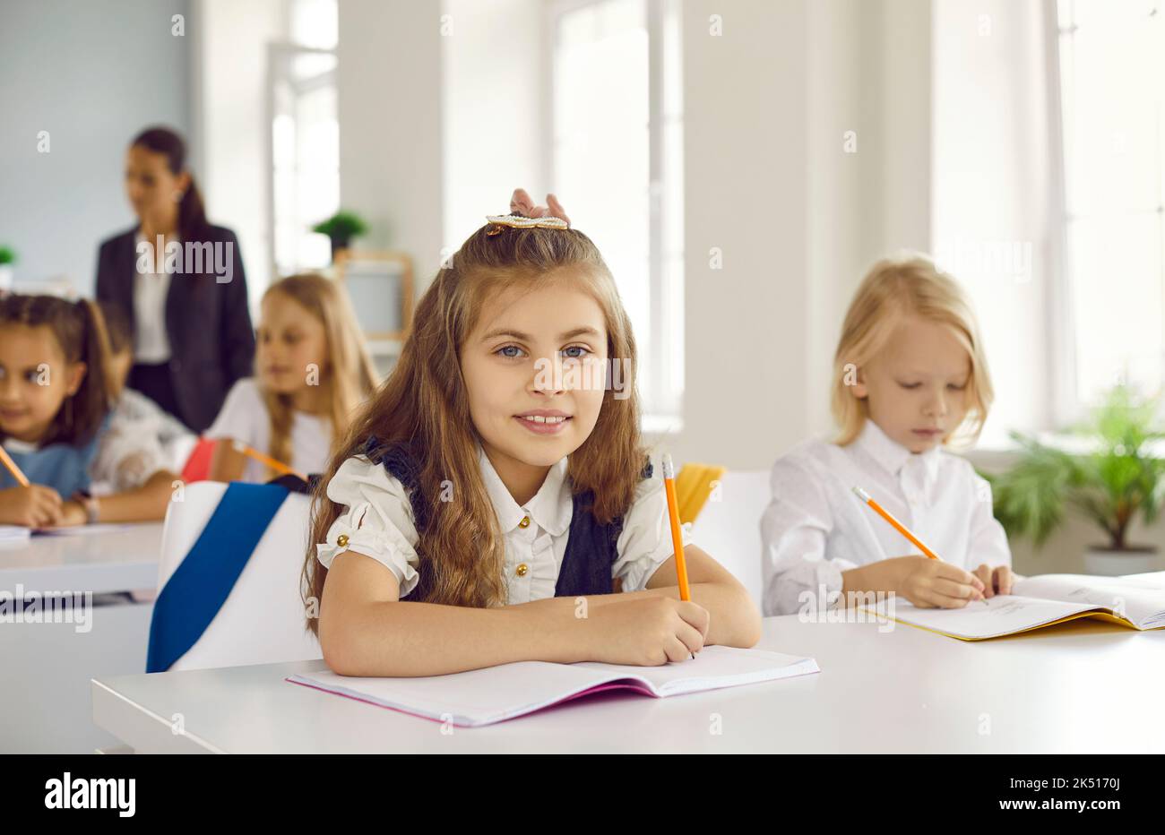 Portrait d'une jolie écolière heureuse assise à son bureau pendant la classe Banque D'Images