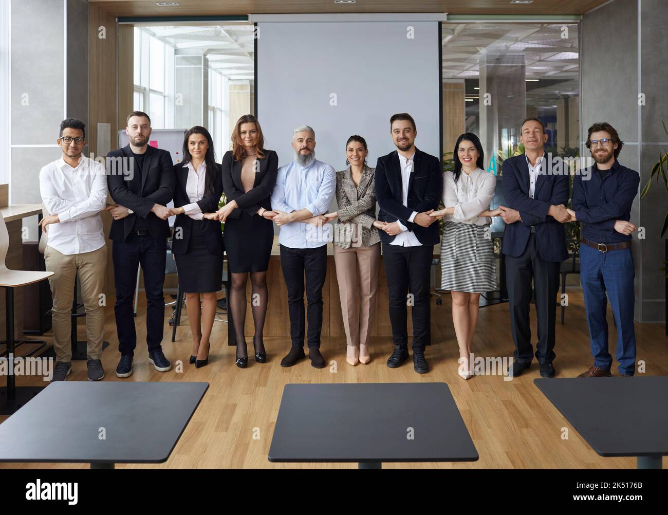 Équipe diversifiée d'employés d'entreprise heureux debout au bureau, tenant les mains et souriant Banque D'Images