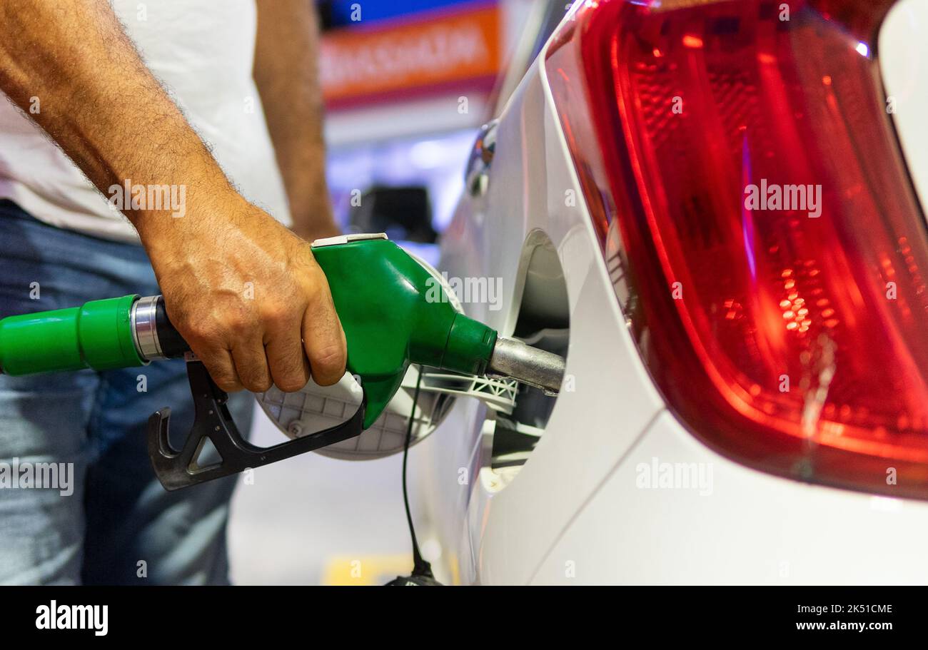 Cachez un chauffeur masculin méconnaissable dans des vêtements décontractés remplissant un réservoir de voiture blanche moderne avec un pistolet à carburant dans une station-service Banque D'Images