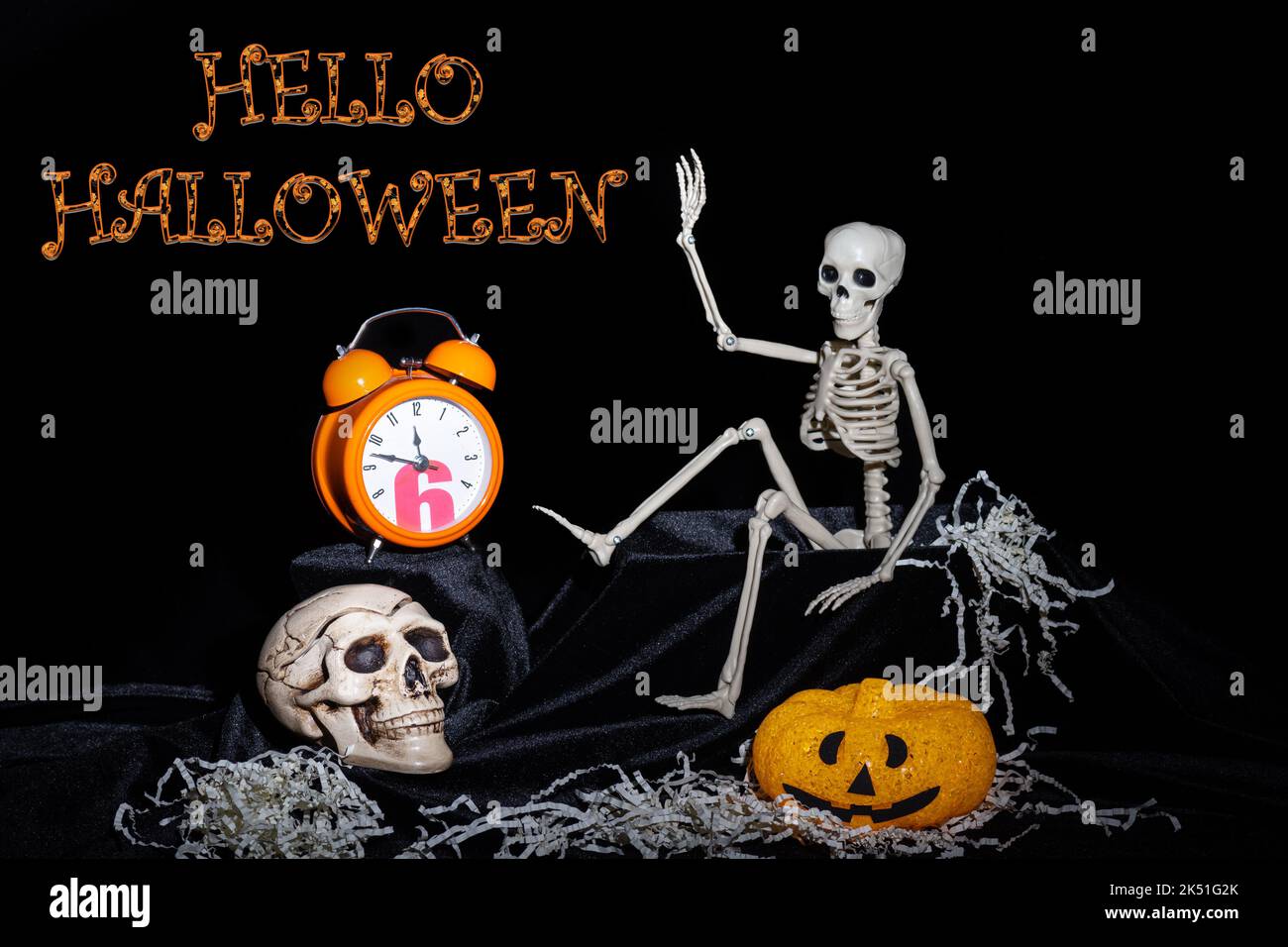 Un squelette jouet rampant hors de la tombe et agitant, salutation, citrouilles avec des grimaces, une horloge orange, un crâne sur un fond noir avec le texte lui Banque D'Images
