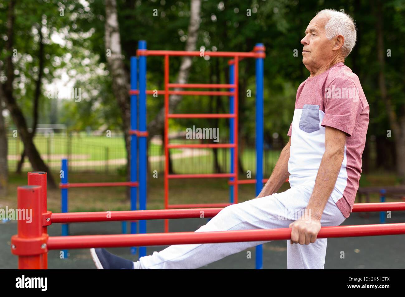 L'homme sportif senior effectue divers exercices sur des barres inégales dans le parc Banque D'Images